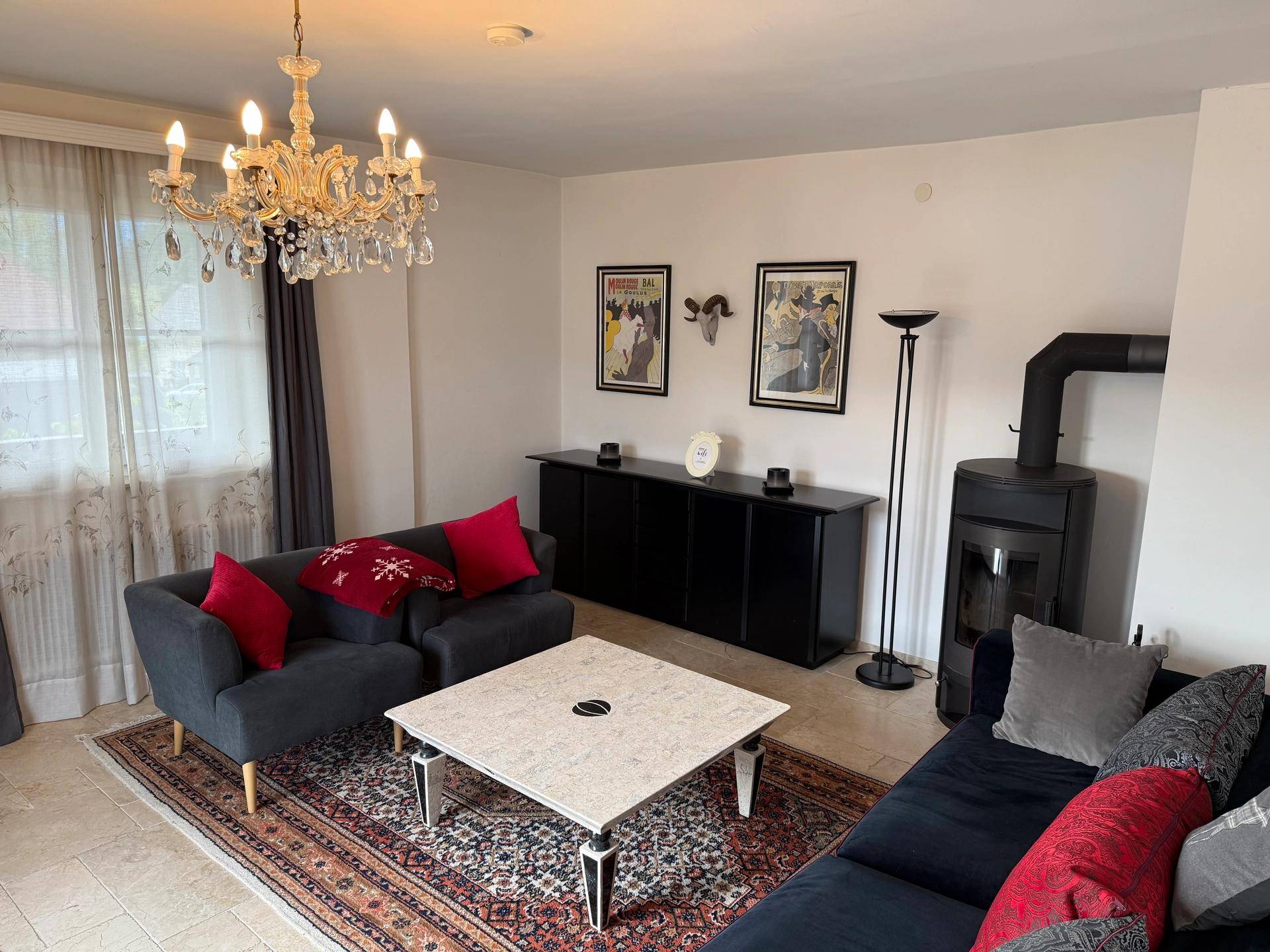 Gemütliches Wohnzimmer mit Kaminofen, bequemen Sofas, einem Kronleuchter und Teppichboden.