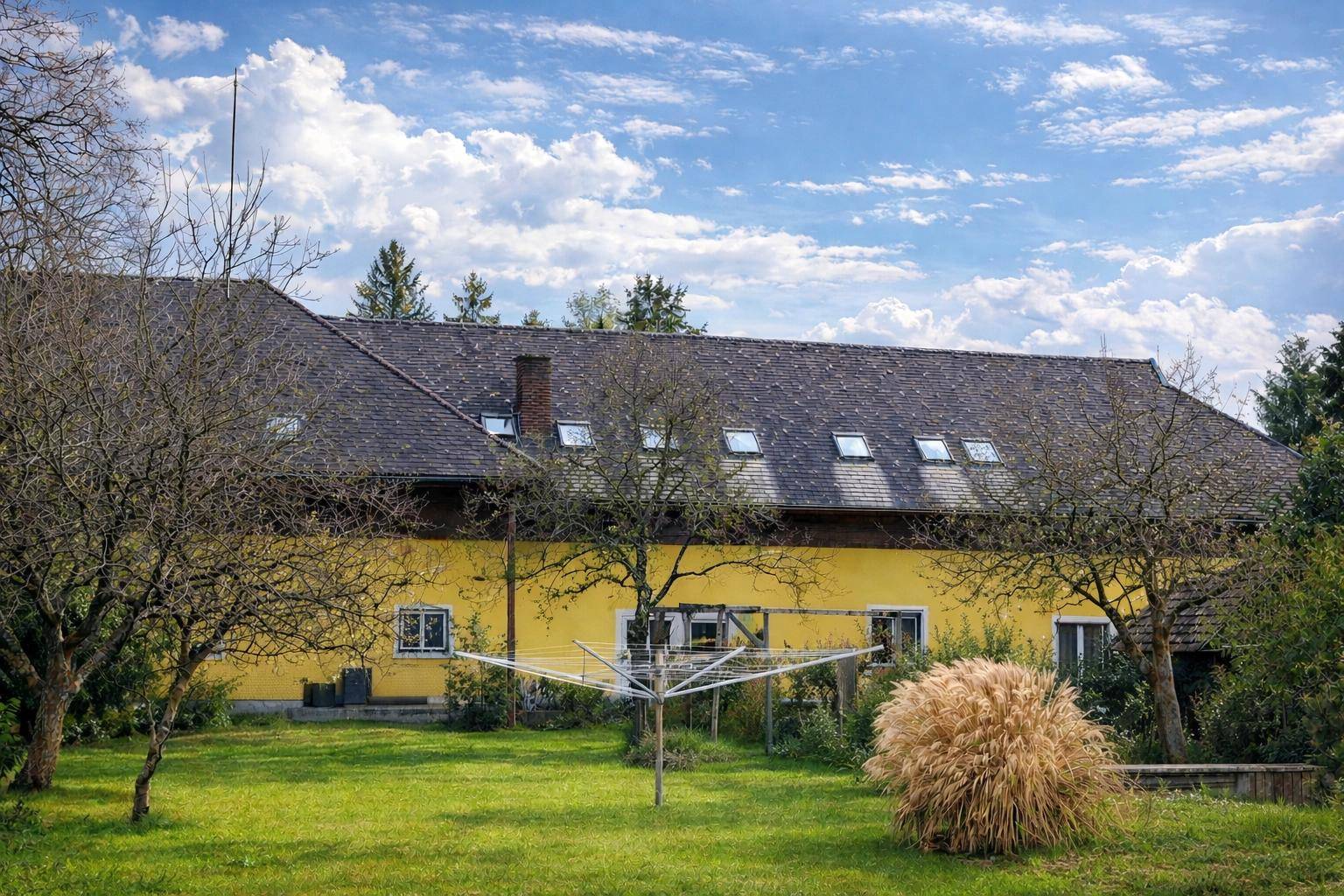 Großzügiger Gartenbereich mit Rasenfläche, Bäumen und dem gelben Gebäude im Hintergrund unter blauem Himmel.