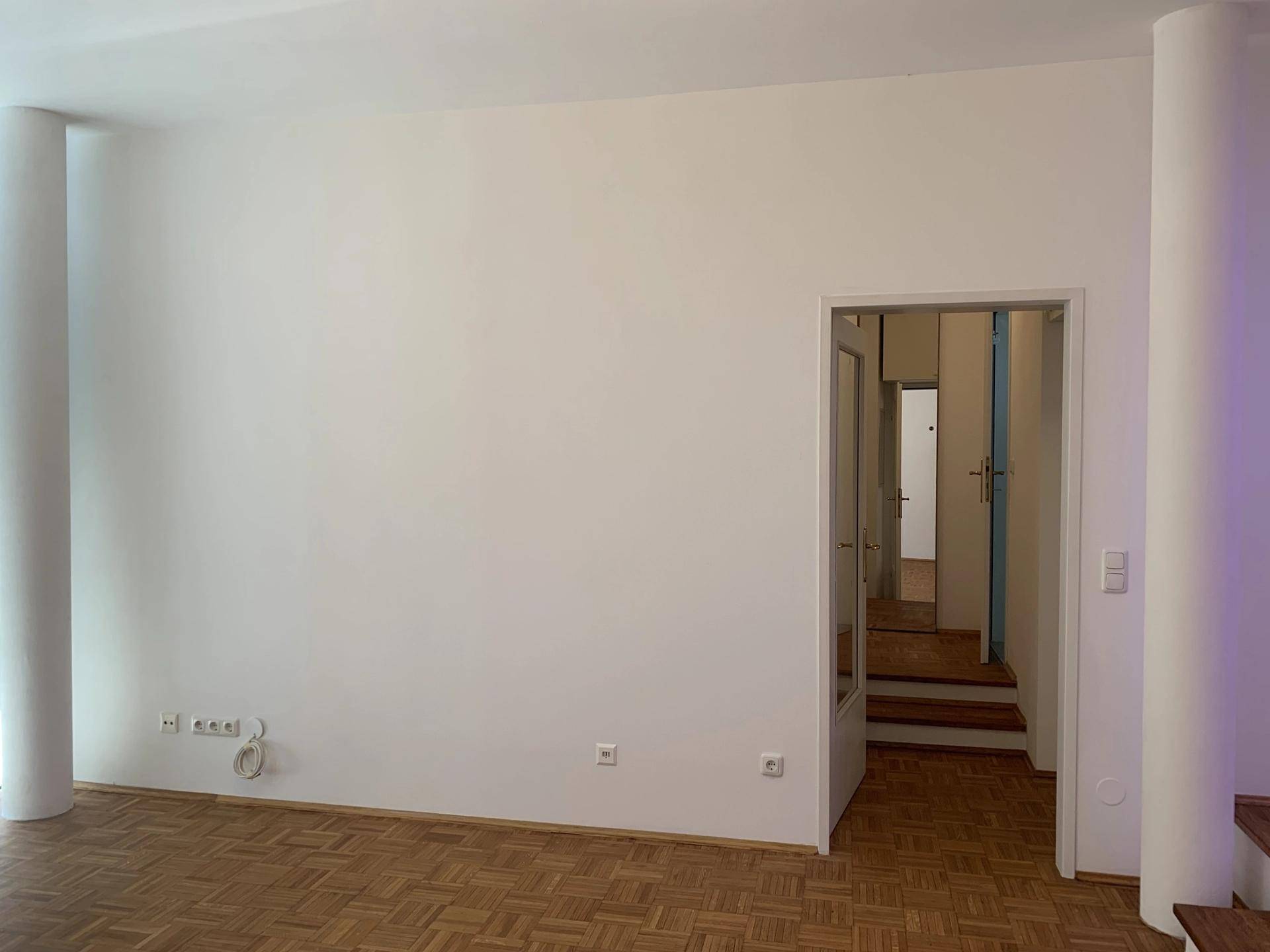 Leeres Zimmer mit Parkettboden und einer Tür, die zu einem weiteren Raum führt.