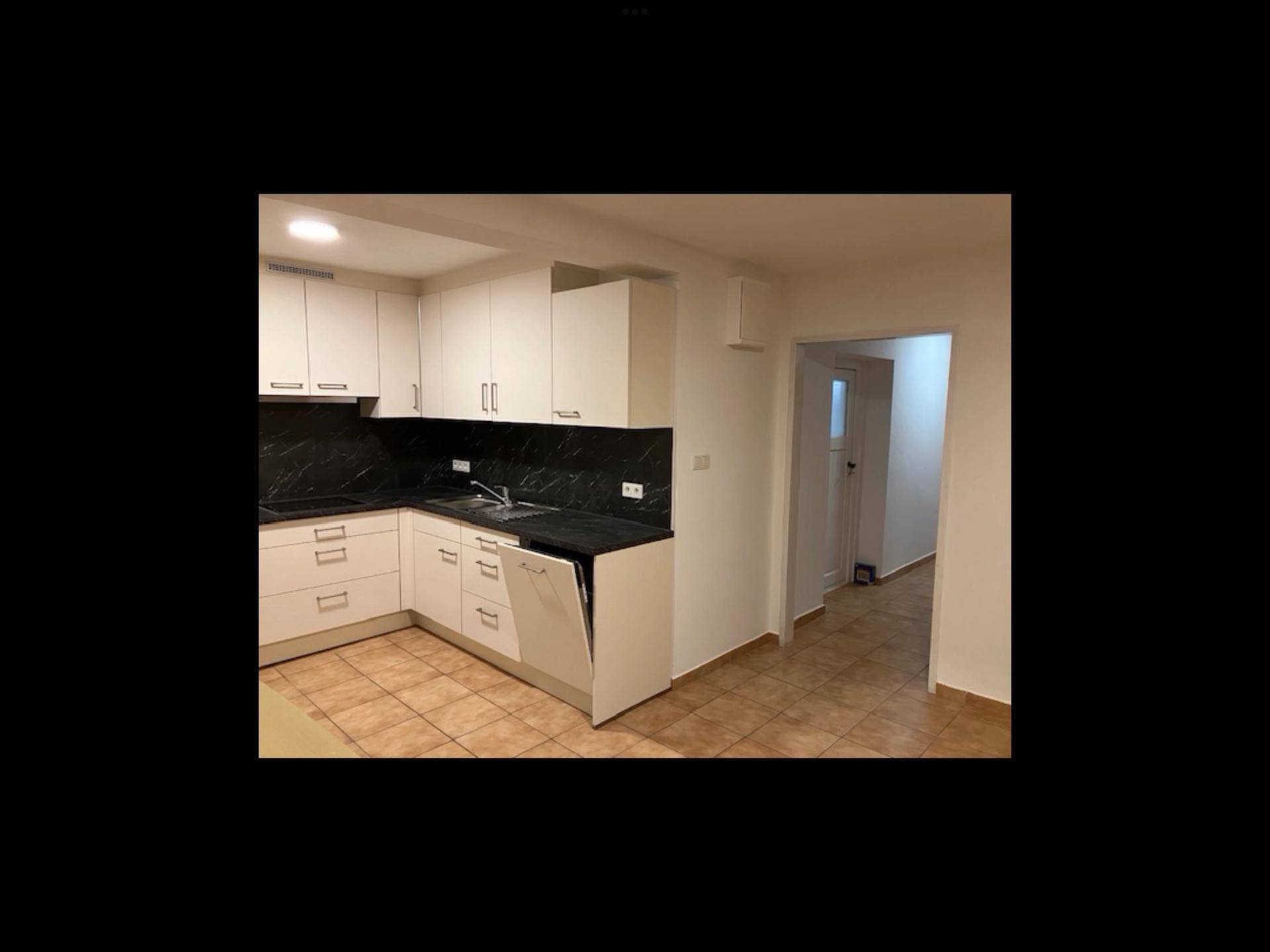 Winkelküche in Weiß mit schwarzen Arbeitsflächen und integrierten Geräten, bereit zur Nutzung.