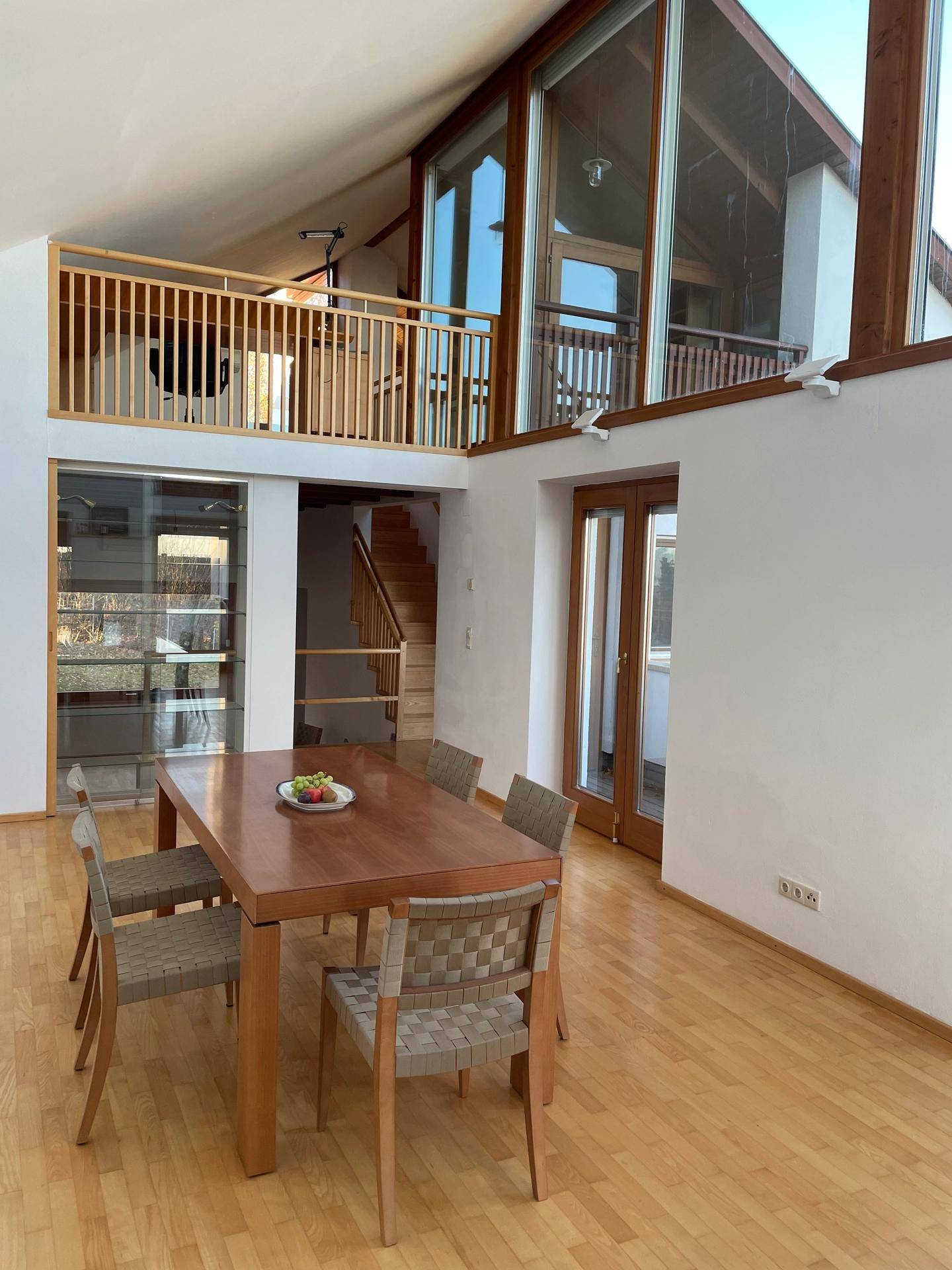 Heller Essbereich mit Holztisch und Stühlen, hohen Decken und großen Fensterfronten.