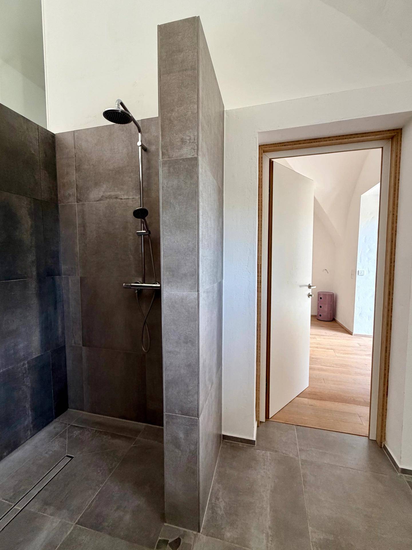 Modernes Badezimmer mit großer begehbarer Dusche und dunklen Fliesen.