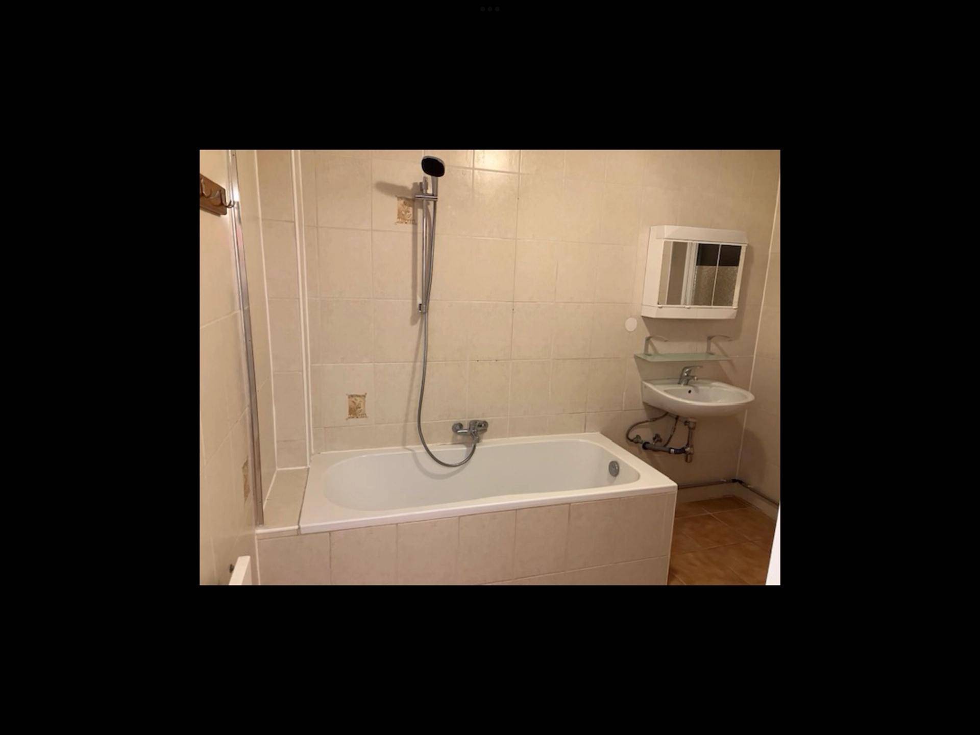 Badezimmer mit Fliesen, Badewanne und Regalen, bereit zur Renovierung.