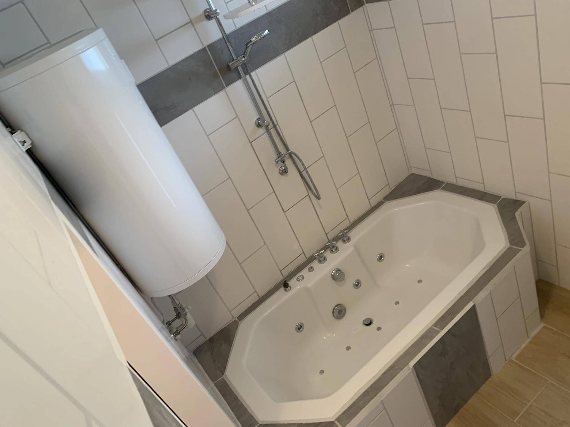 Modernes Badezimmer mit einer Eckbadewanne, Duschvorrichtung und hellen Fliesen.