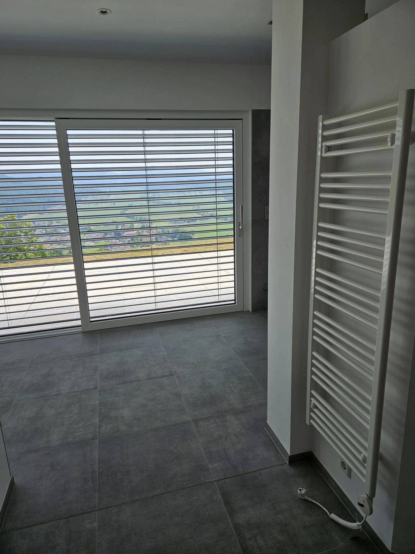 Modernes Badezimmer mit grauen Fliesen, Handtuchheizkörper und großen Fenstern mit Landschaftsblick.