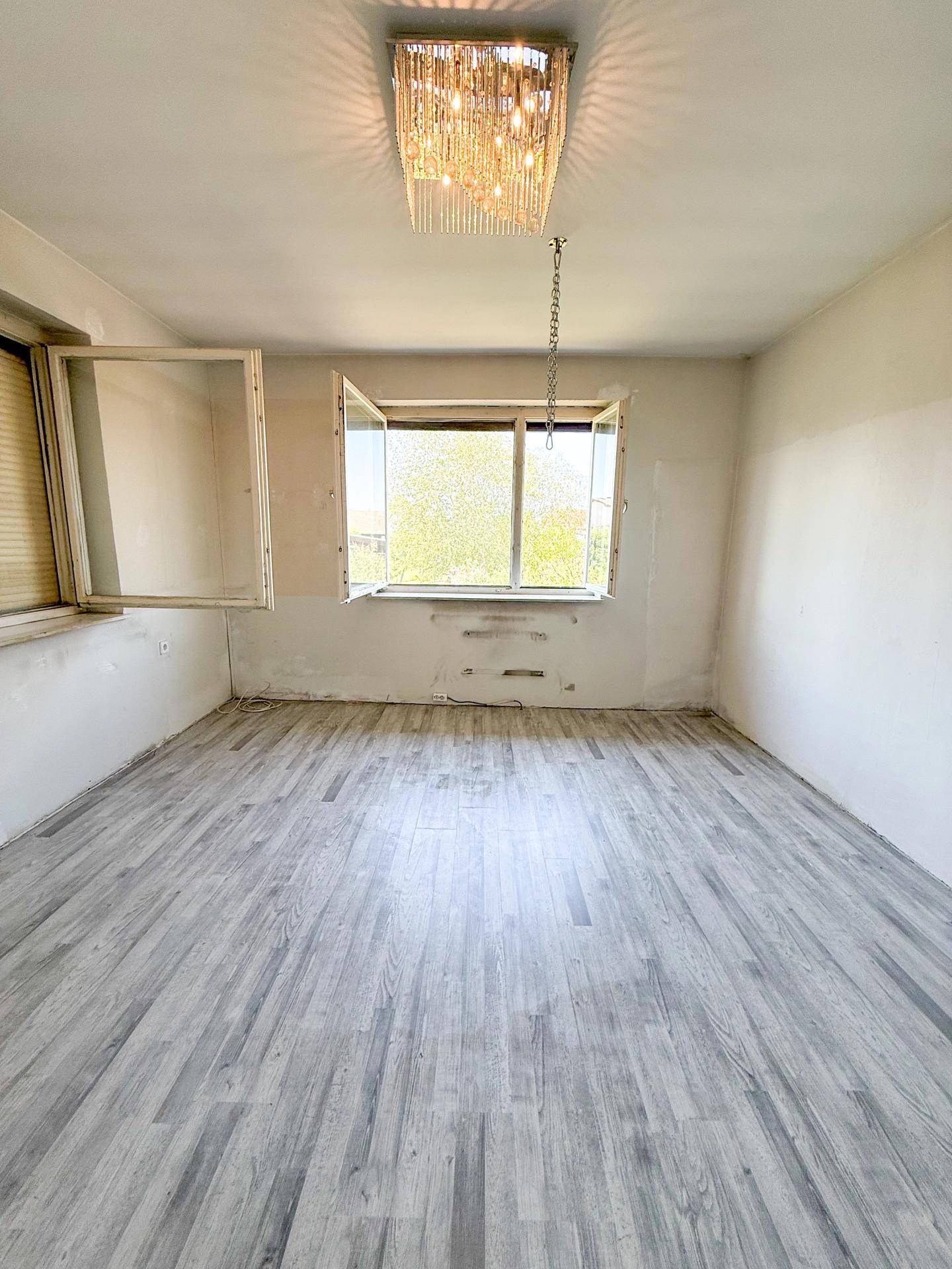 Leeres Zimmer mit grauem Laminatboden und geöffneten Fenstern, bereit für Renovierung.