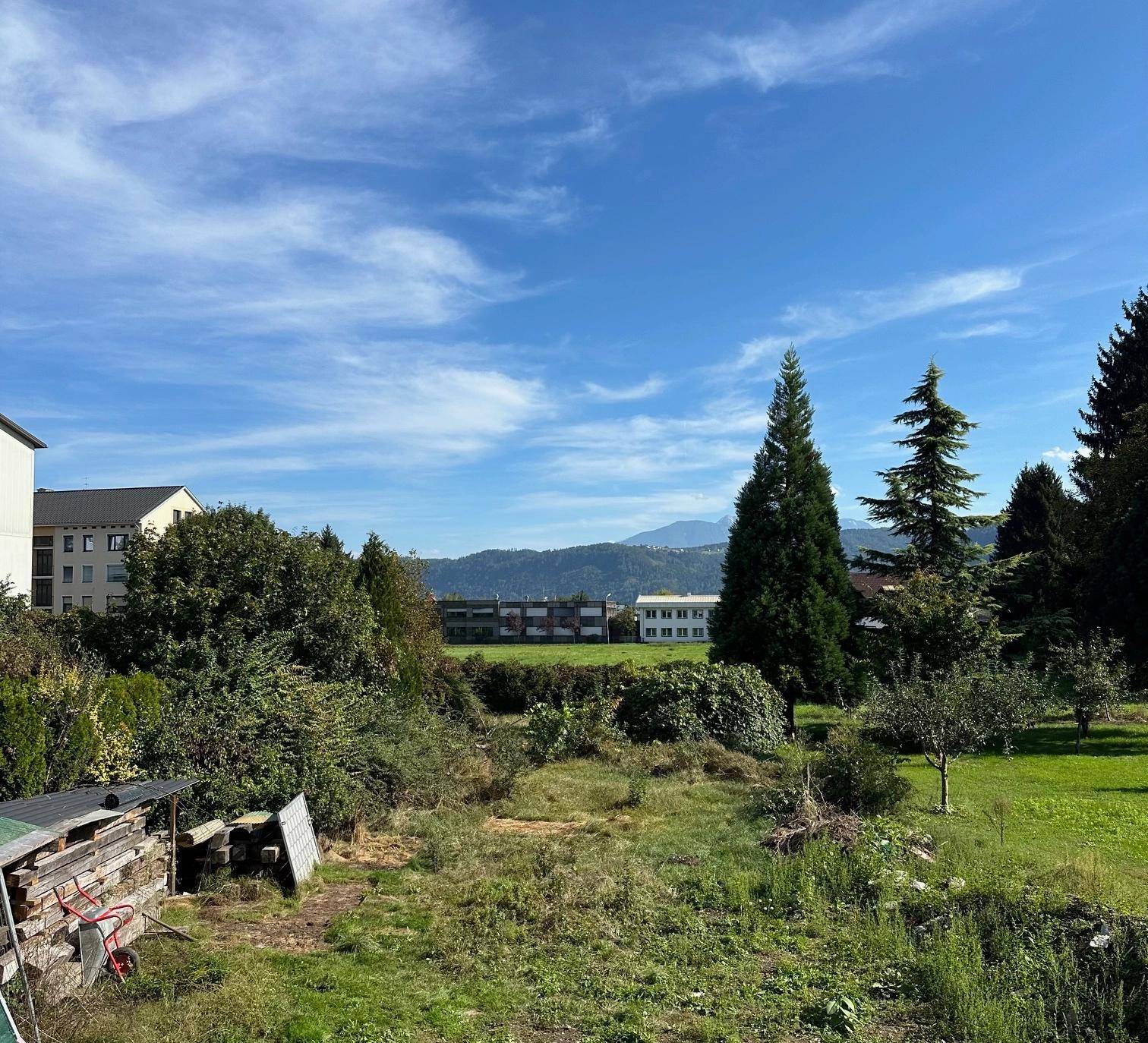Weitläufiges grünes Grundstück mit Baumbestand und einer malerischen Bergkulisse am Horizont.