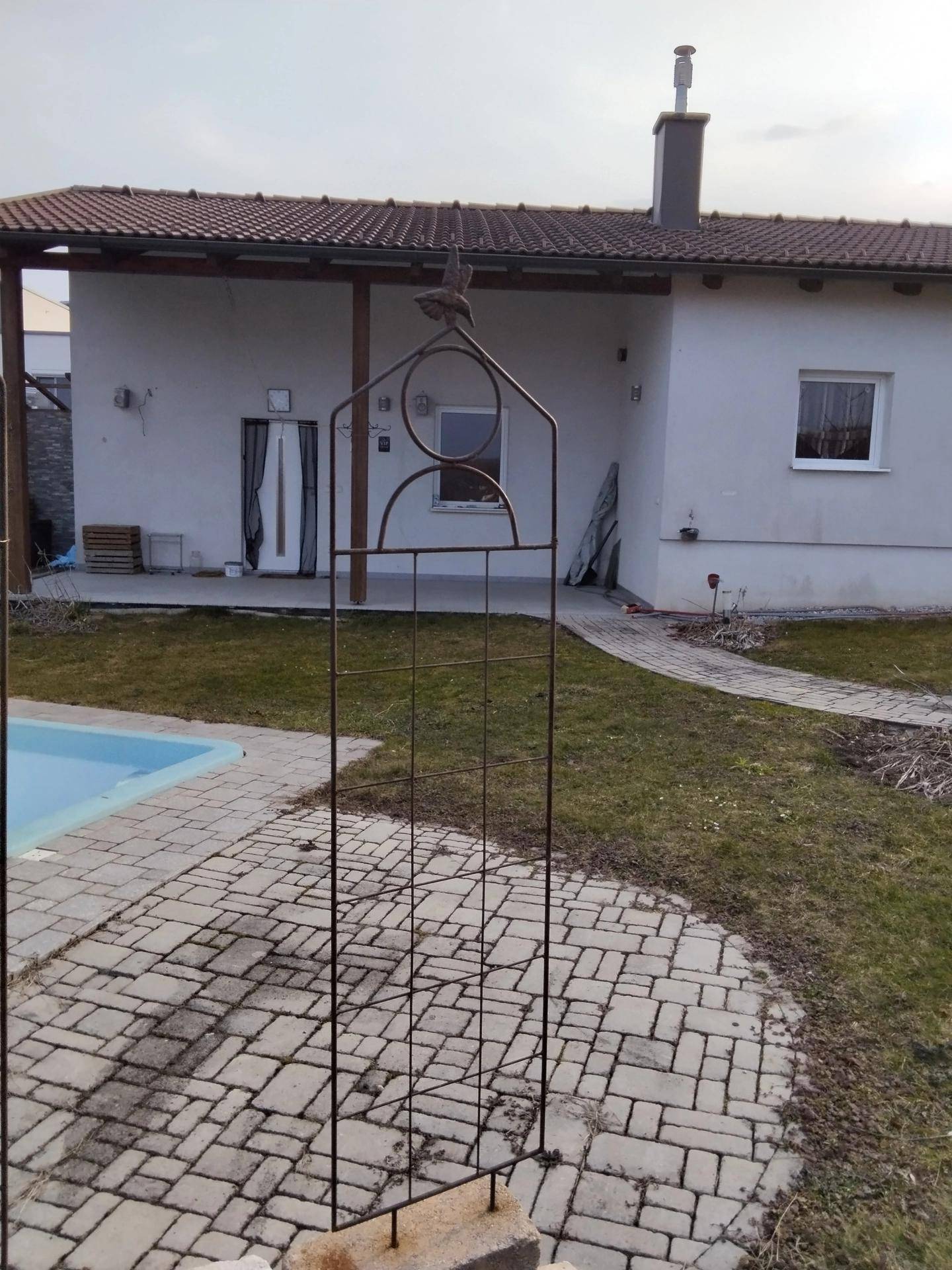Gartenbereich mit Pool und einem Metallspalier vor dem Wohnhaus.