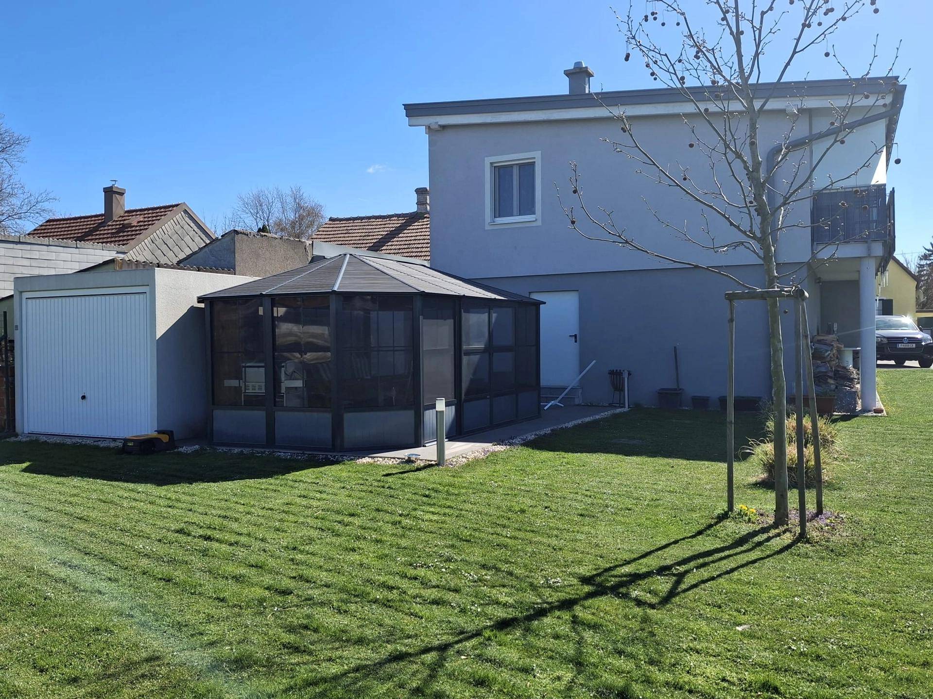 Ansicht des Hauses von der Seite mit Rasenfläche, Wintergarten und einer separaten Garage.