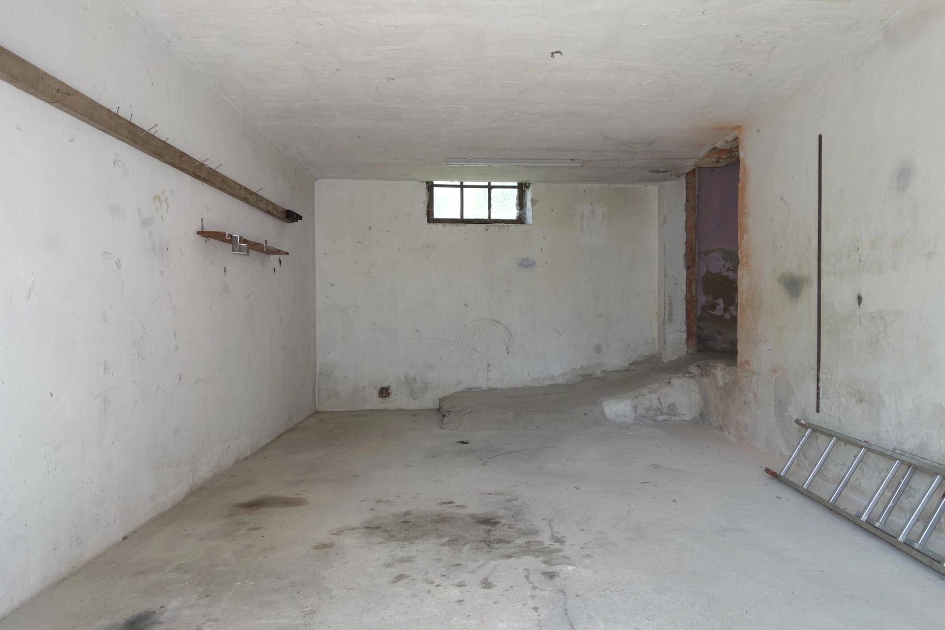 Leerer Garagenraum mit weiß gestrichenen Wänden, einem kleinen Fenster und einer Leiter.