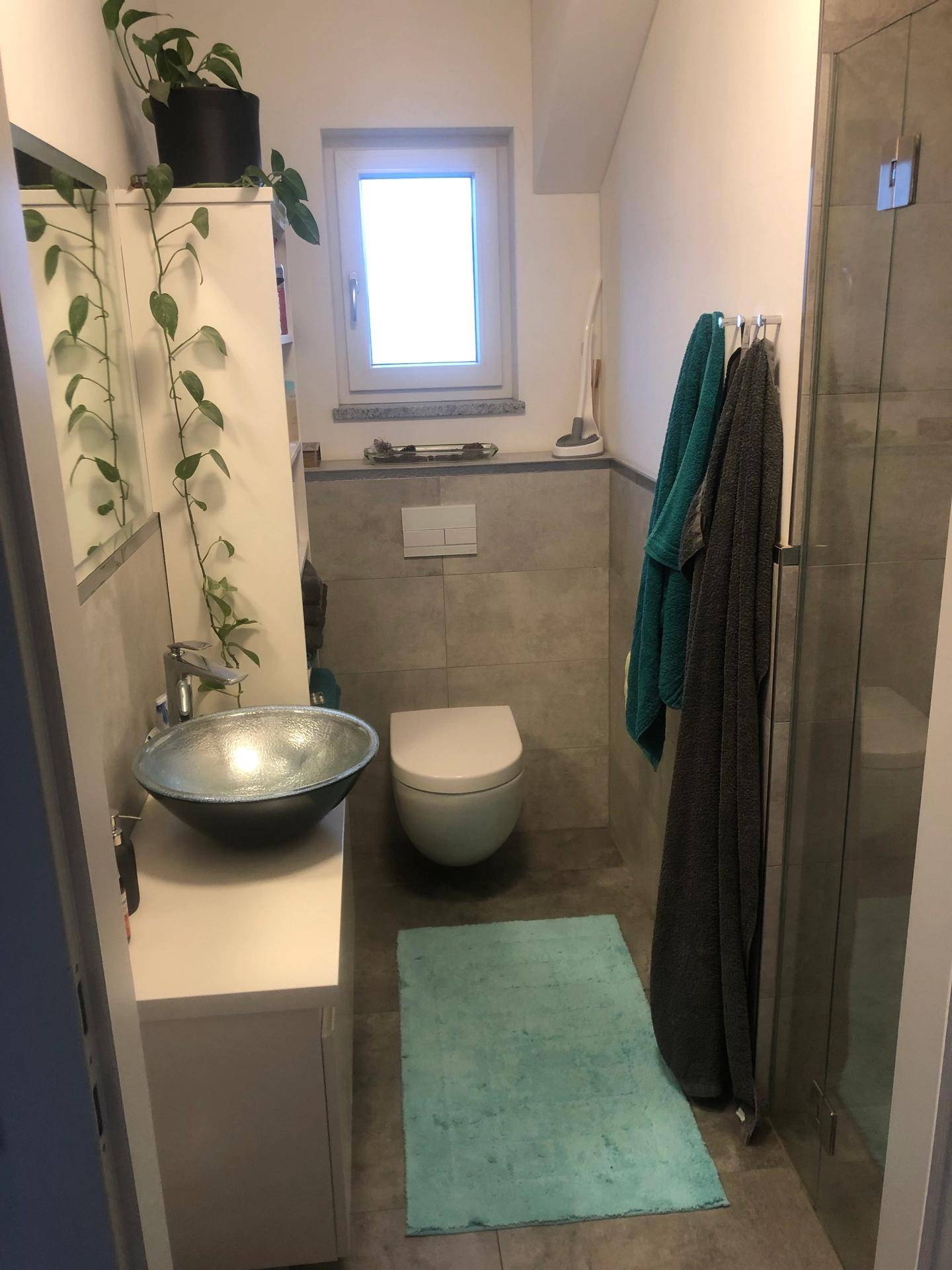 Helles Badezimmer mit Toilette, Waschbecken, Duschkabine und Fenster.