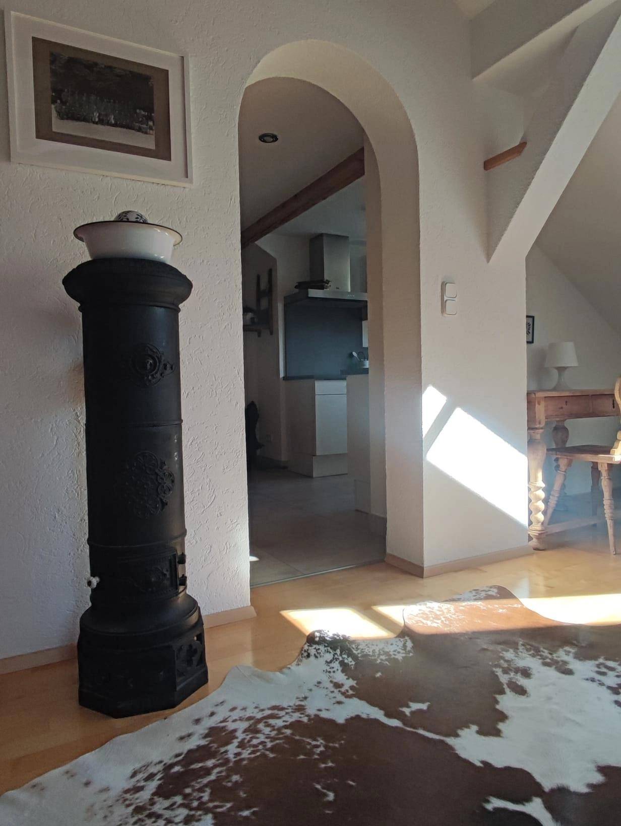 Gemütlicher Wohnbereich mit traditionellem Ofen, Holzboden und offenem Zugang zur Küche.