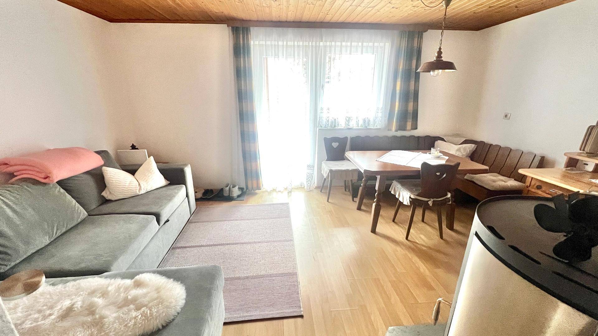 Gemütlicher Wohn-Essbereich mit Sofa, Eckbank und einem traditionellen Holzofen im Vordergrund.