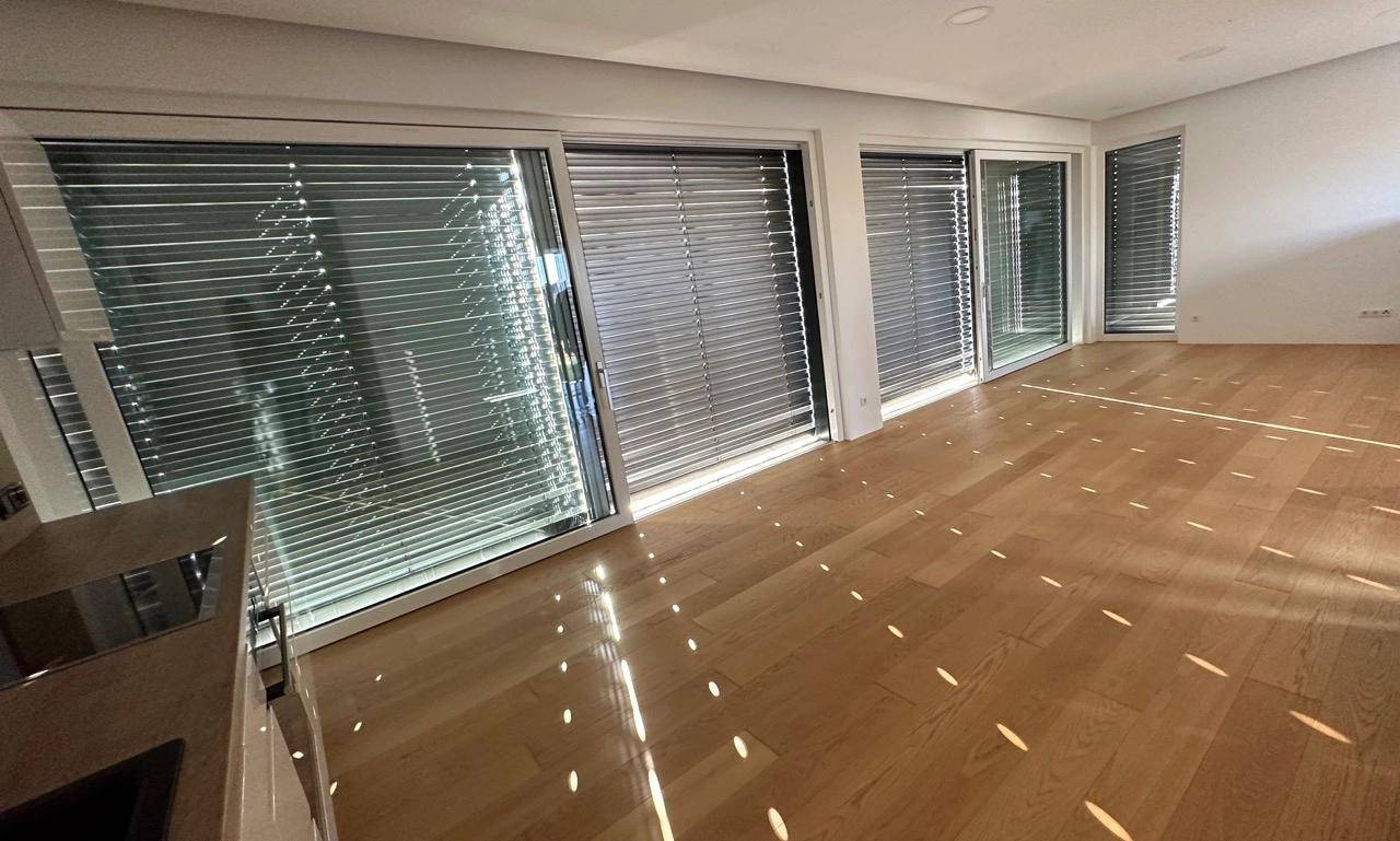 Heller Wohnbereich mit Holzboden und großen Fenstern, ausgestattet mit modernen Jalousien für Privatsphäre.
