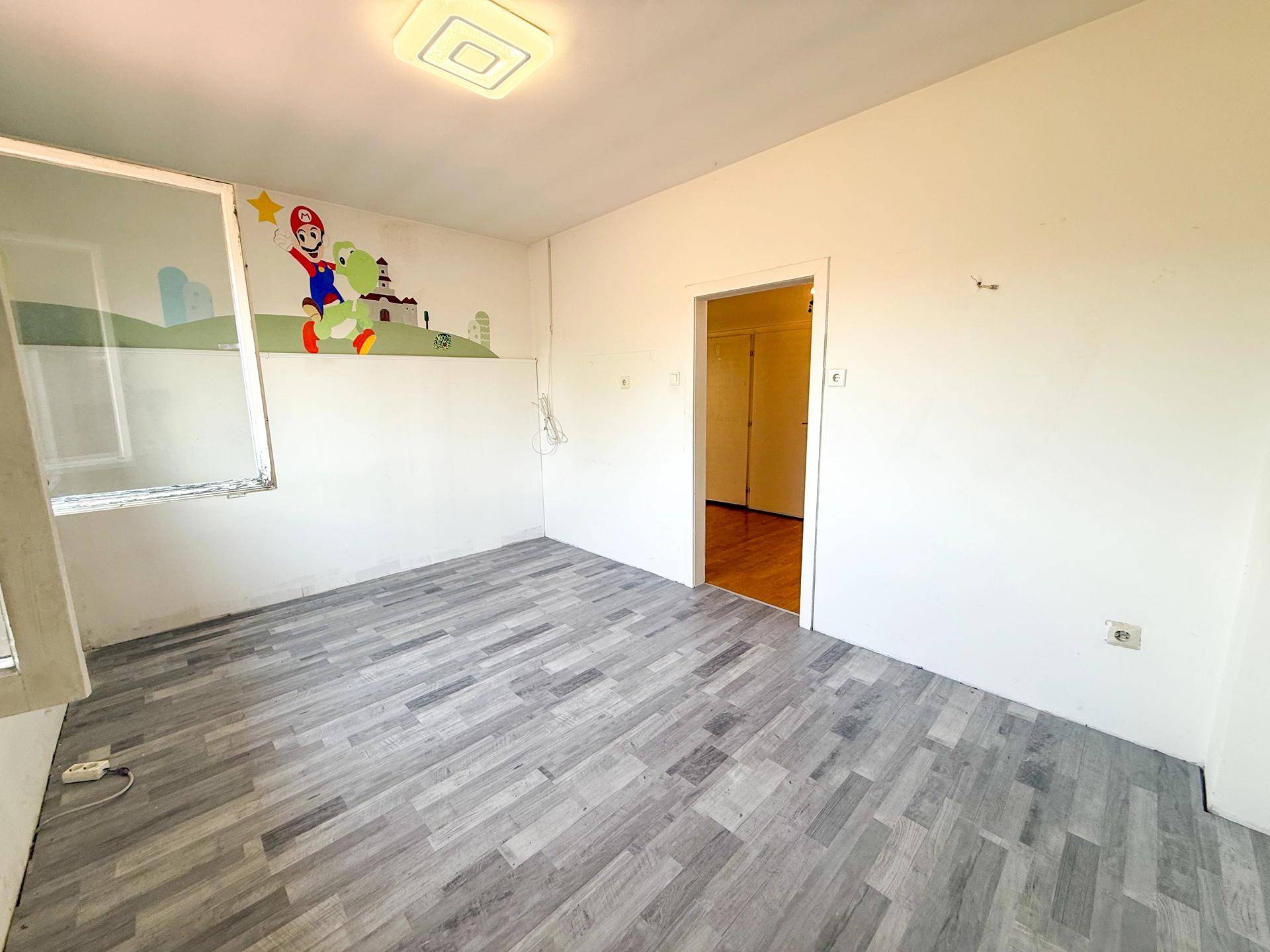 Kinderzimmer mit grauem Laminatboden, weiß gestrichenen Wänden und bunter Wanddekoration.