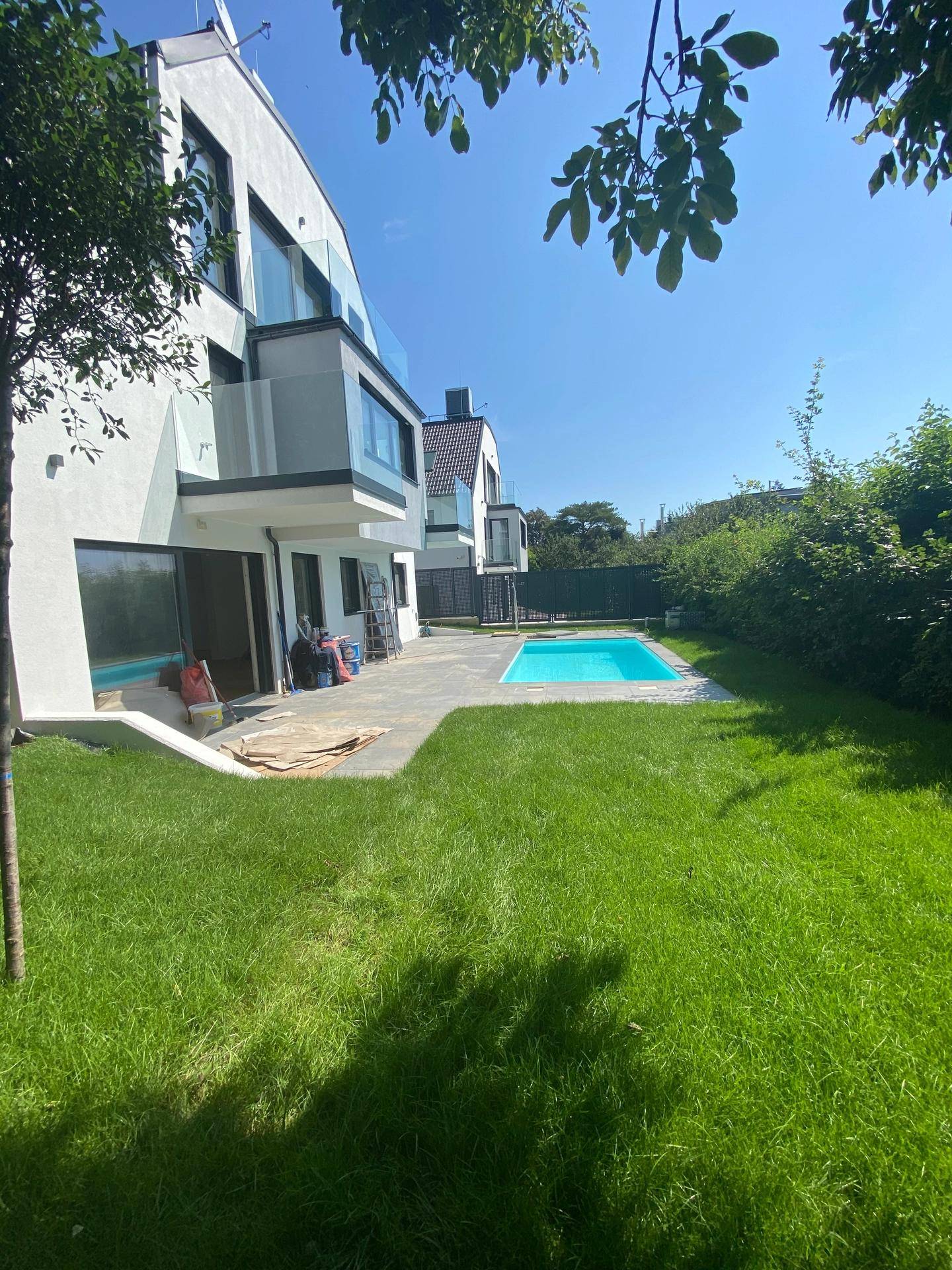Gartenbereich mit Rasenfläche, Pool und gepflasterter Terrasse, noch im Bau.