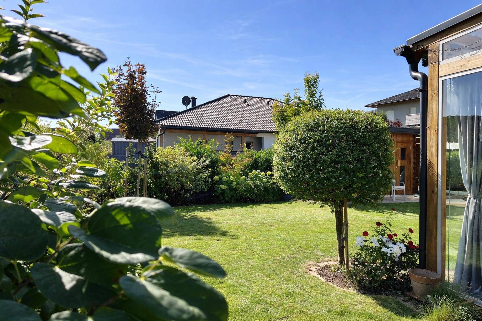 Großer, gepflegter Garten mit Rasen, Sträuchern und Blick auf das Nachbarhaus.