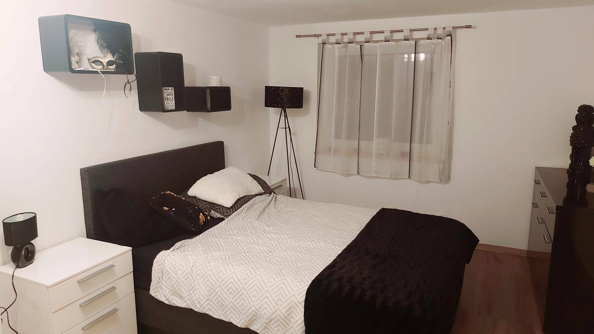 Modernes Schlafzimmer mit dunklem Bett, Nachttischen und einem Fenster mit Vorhängen.