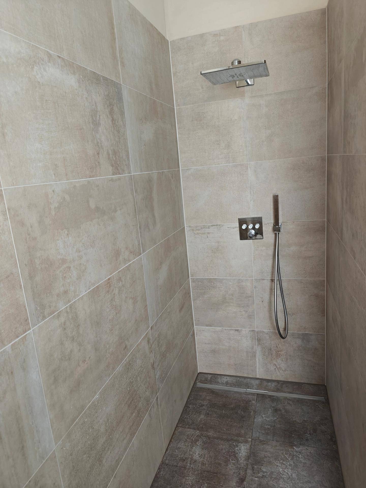 Geräumige, ebenerdige Dusche mit Regenduschkopf und modernen Fliesen.
