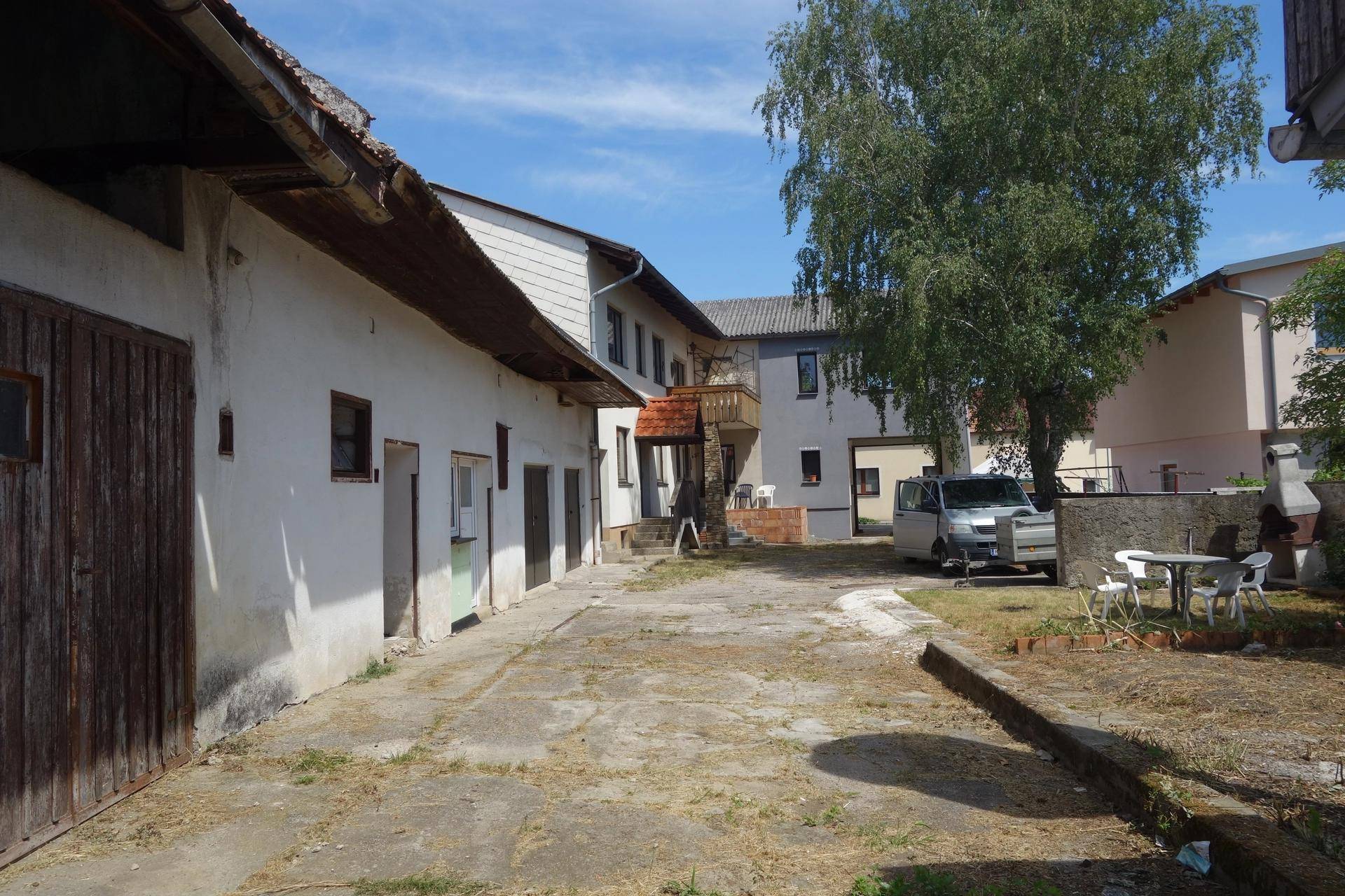 Großer Innenhof mit mehreren Gebäuden, einem Baum, einem Van und einem Grillplatz mit Sitzgelegenheiten.