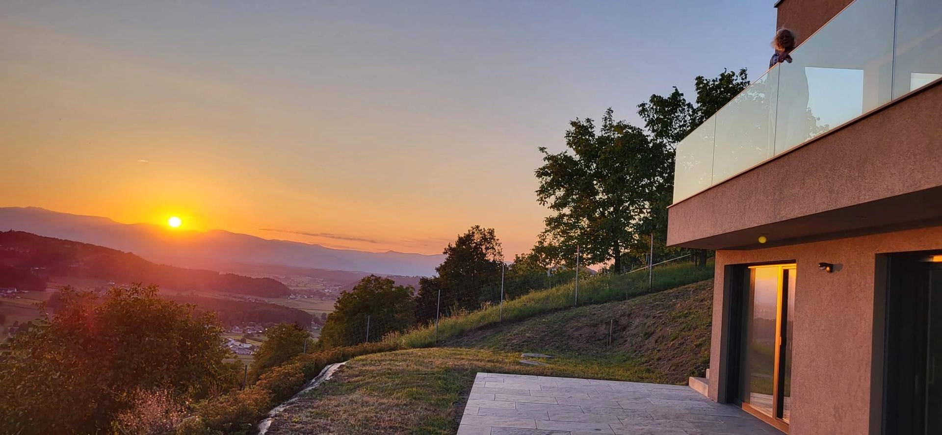 Moderner Balkon mit Glasgeländer und atemberaubendem Blick auf die hügelige Landschaft bei Sonnenuntergang.
