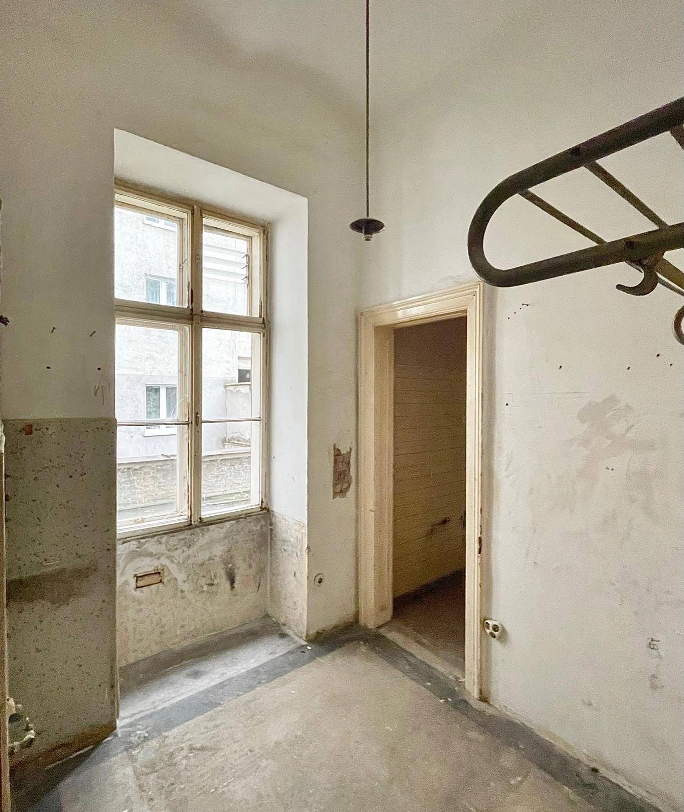 Langer Flur in sanierungsbedürftigem Zustand mit Fenster am Ende und freigelegten Wandbereichen.