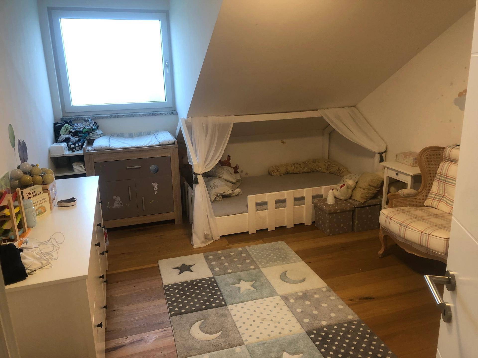 Helles Kinderzimmer mit Dachschräge, Holzboden und einem Kinderbett mit Baldachin.