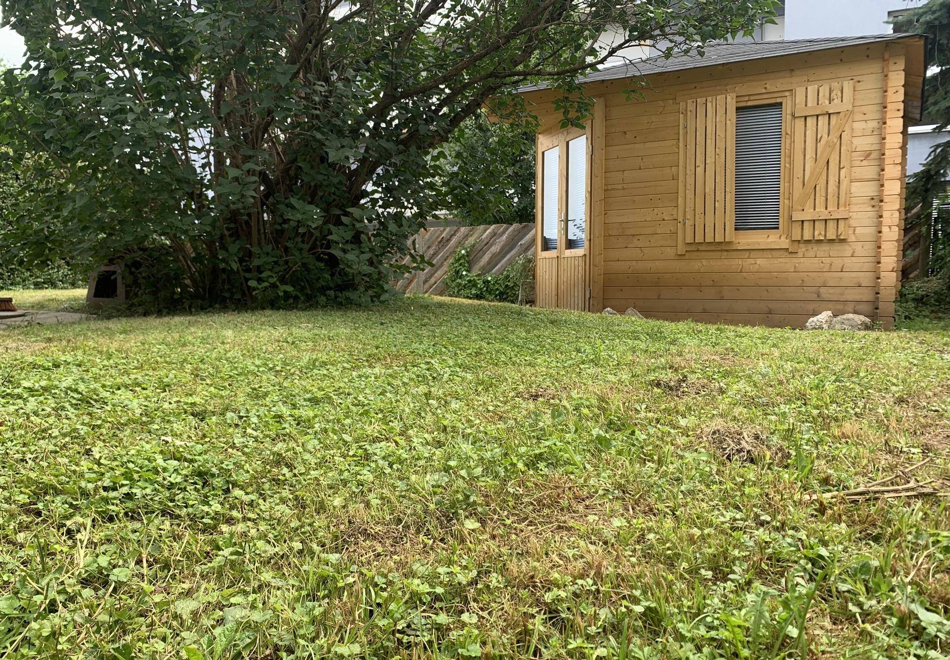 Gepflegter Garten mit Rasenfläche und einem charmanten Holzgartenhaus im Hintergrund.