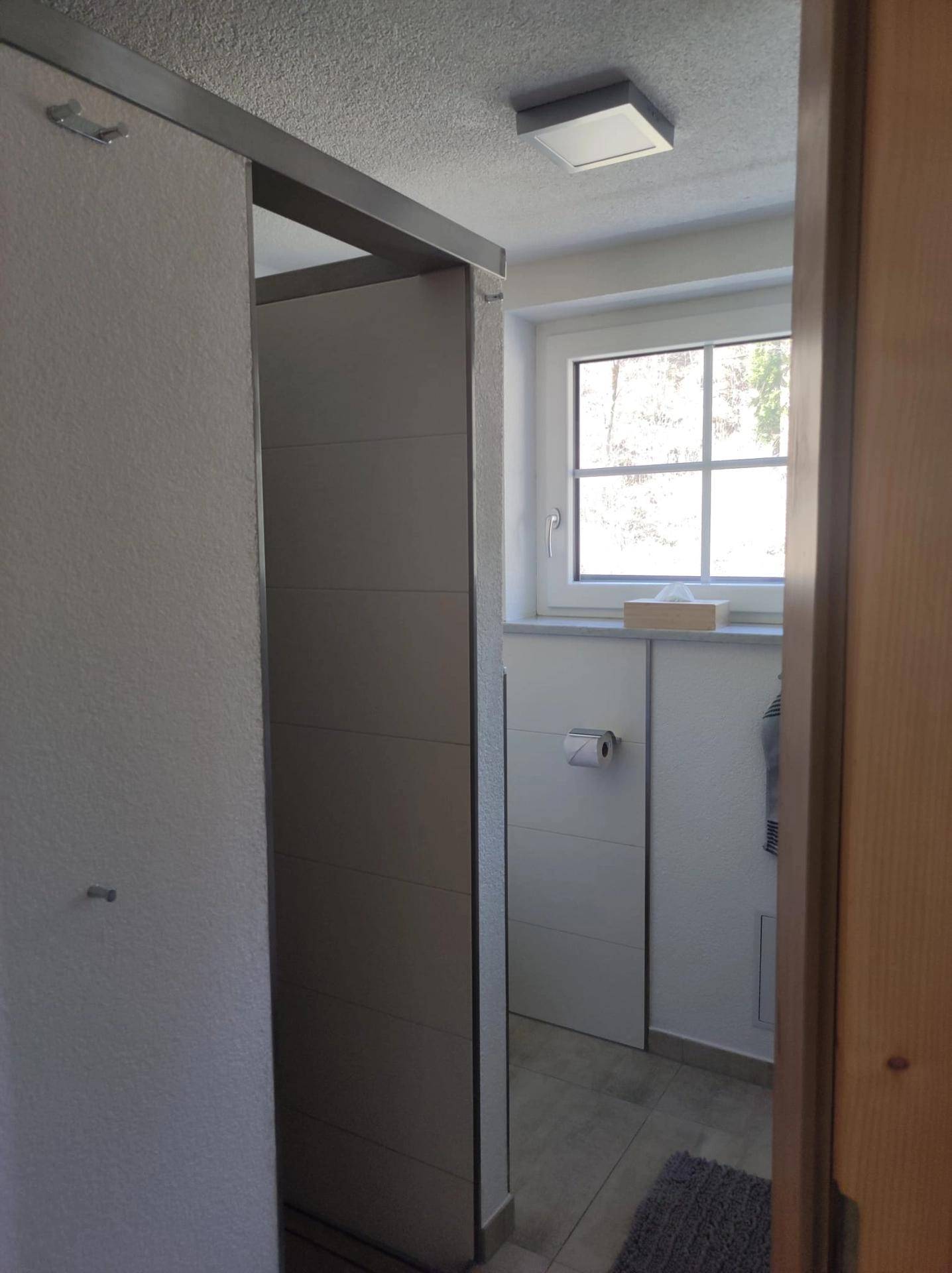 Badezimmer mit Duschbereich, Fenster und hellen Fliesen, gut beleuchtet.