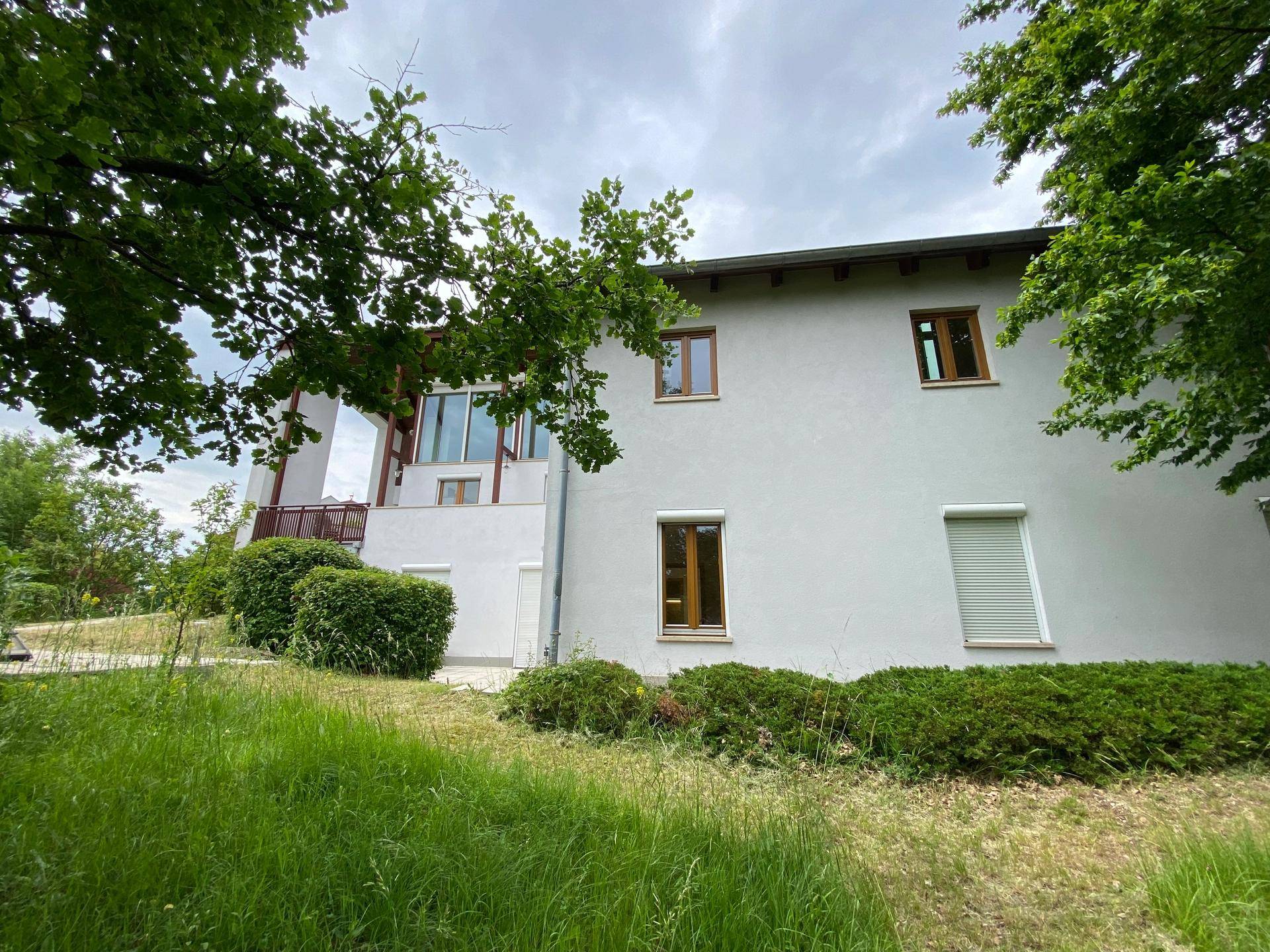 Seitenansicht des Hauses mit weißer Fassade, Fenstern und grüner Umgebung.