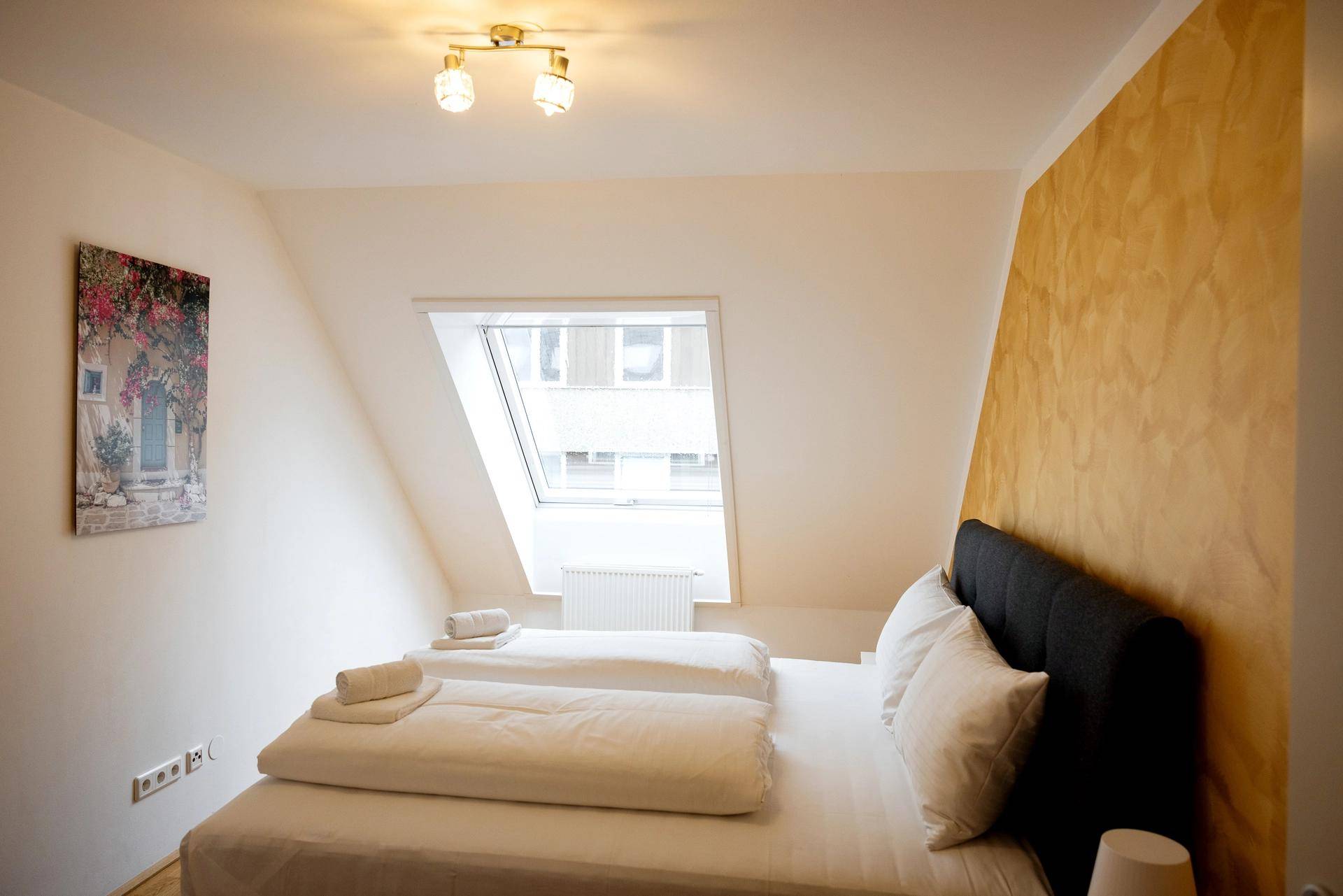 Helles Schlafzimmer mit Doppelbett, Dachfenster und Kunst an der Wand.