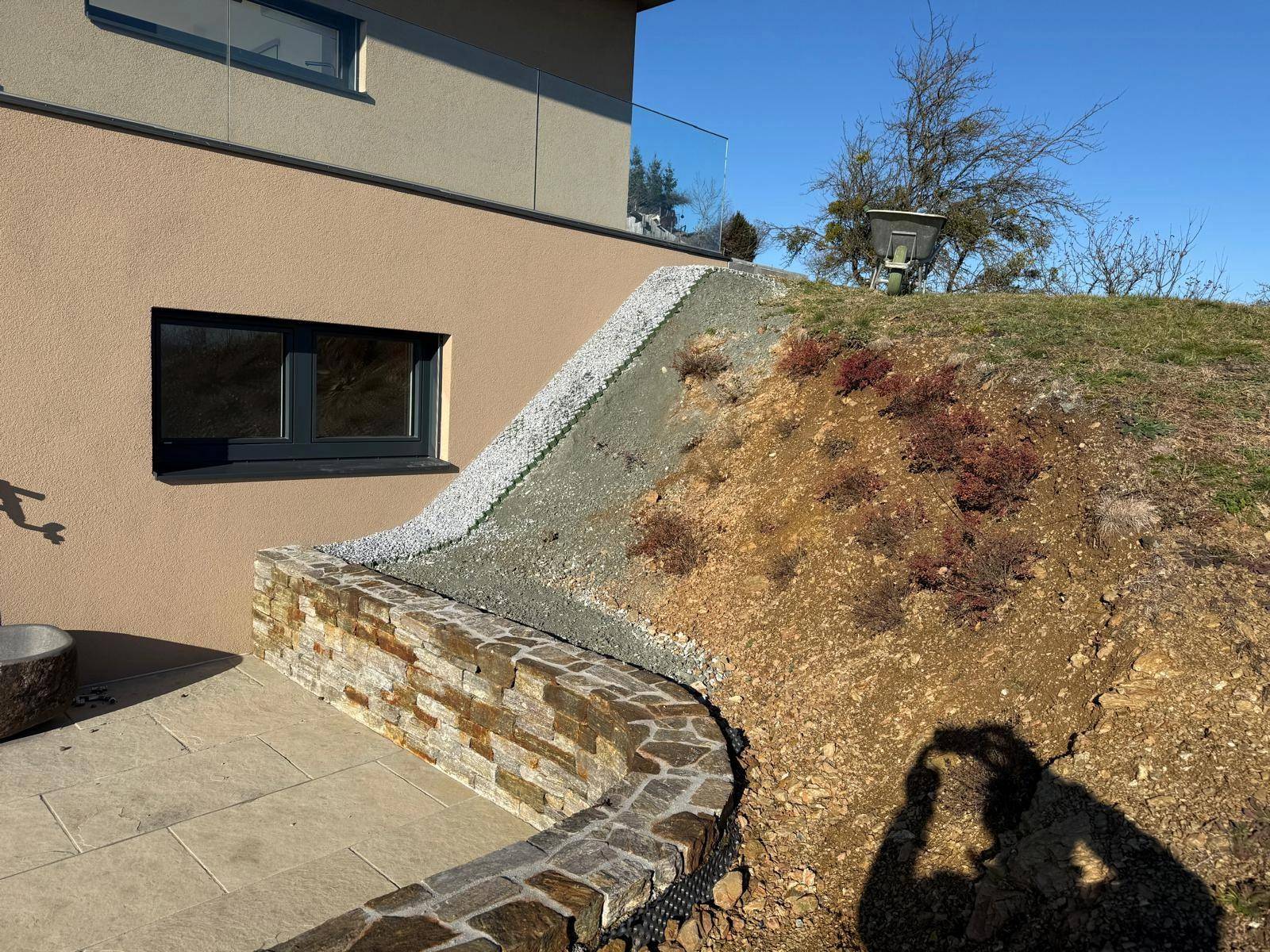Gestalteter Gartenbereich mit Natursteinmauer und Kiesbett, angrenzend an die moderne Hausfassade.