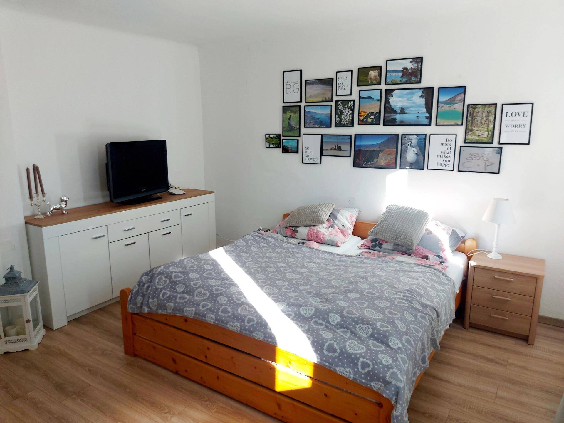 Helles Schlafzimmer mit Holzbett, Laminatboden und einer Bildergalerie an der Wand.