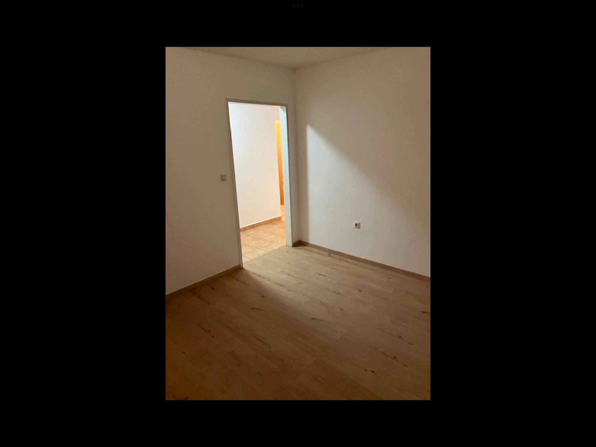 Leeres Zimmer mit Holzboden, Fenster und Heizkörper, bereit zur individuellen Gestaltung.