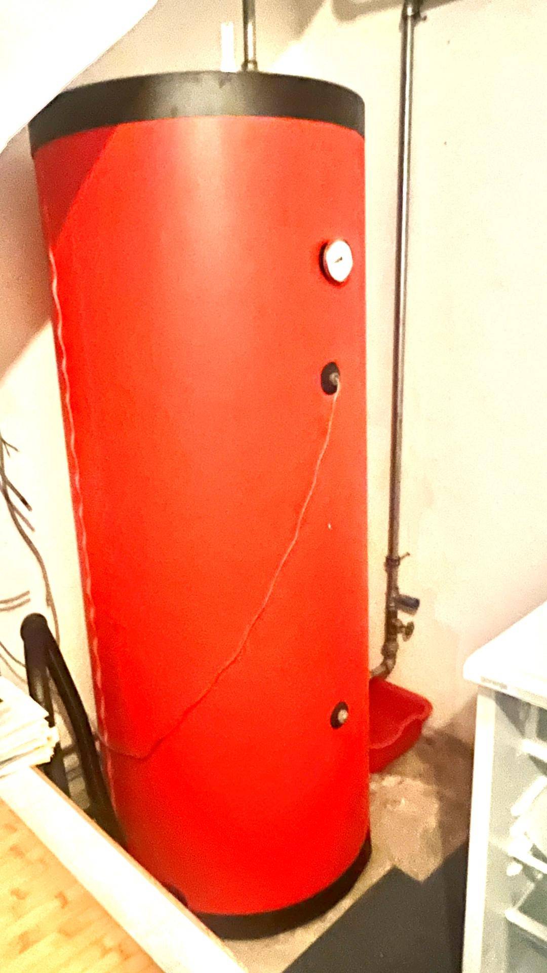 Großer roter Warmwasserspeicher in einem Technikraum oder Kellerbereich.