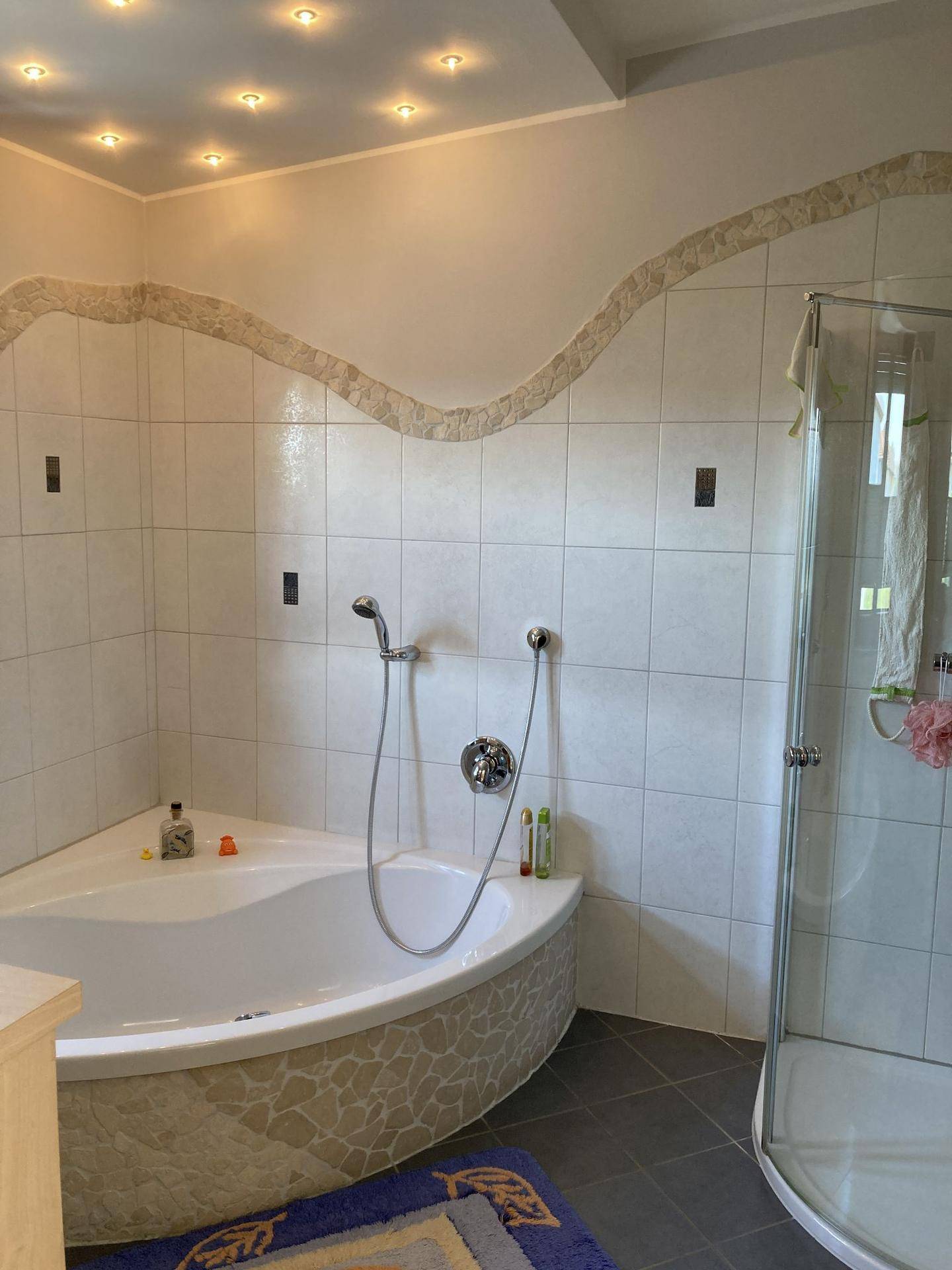Badezimmer mit Eckbadewanne, Duschkabine und Einbaustrahlern an der Decke.