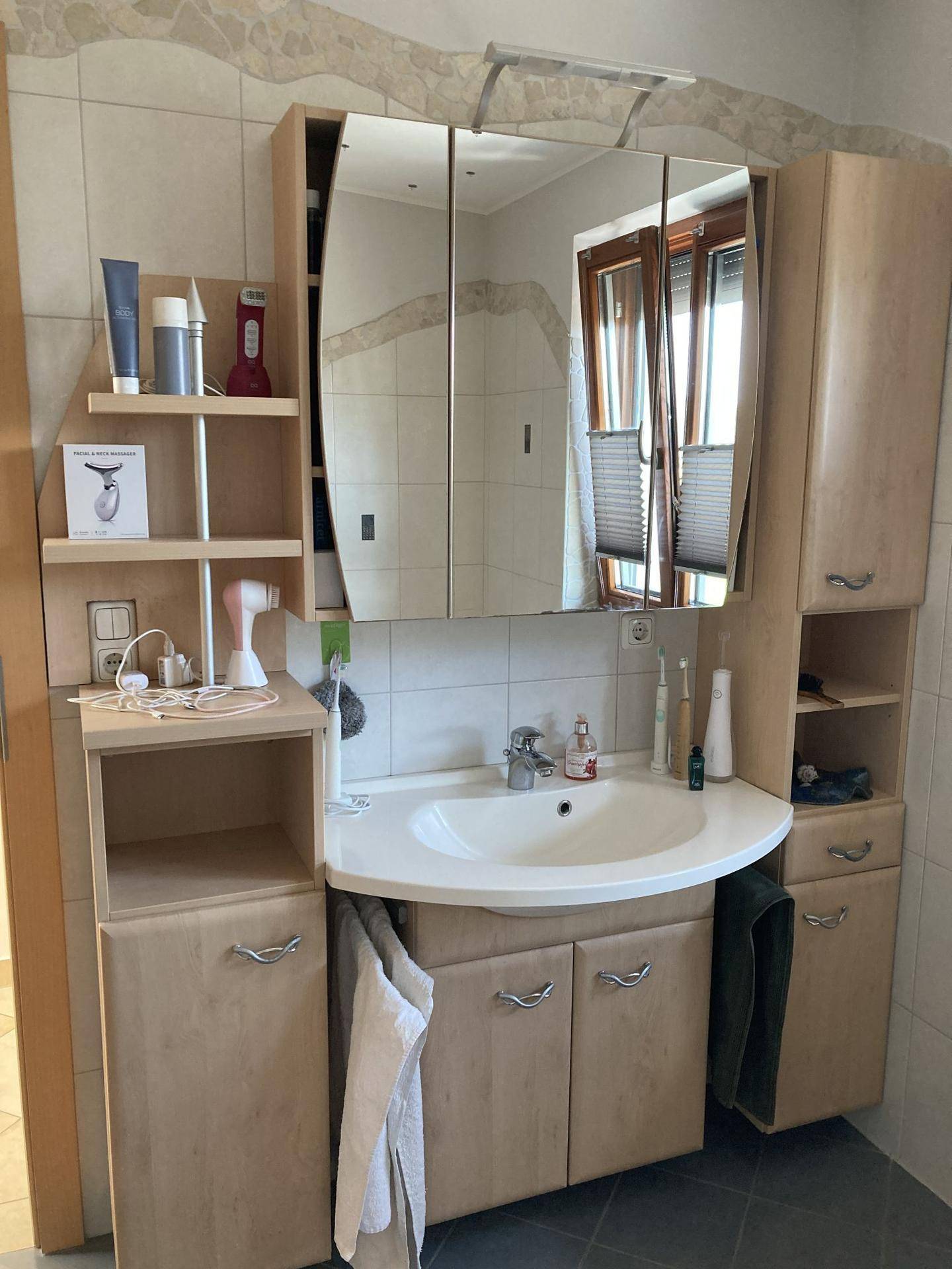 Badezimmer mit Waschtischunterschrank, Spiegelschrank und Fenster.