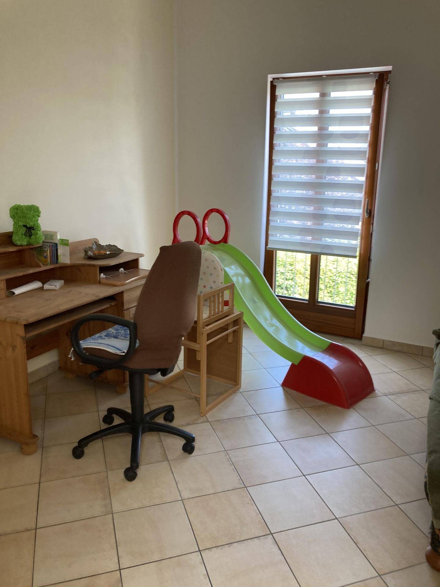 Arbeitszimmer mit Holzschreibtisch, Bürostuhl und einem kleinen Spielgerät am Fenster.
