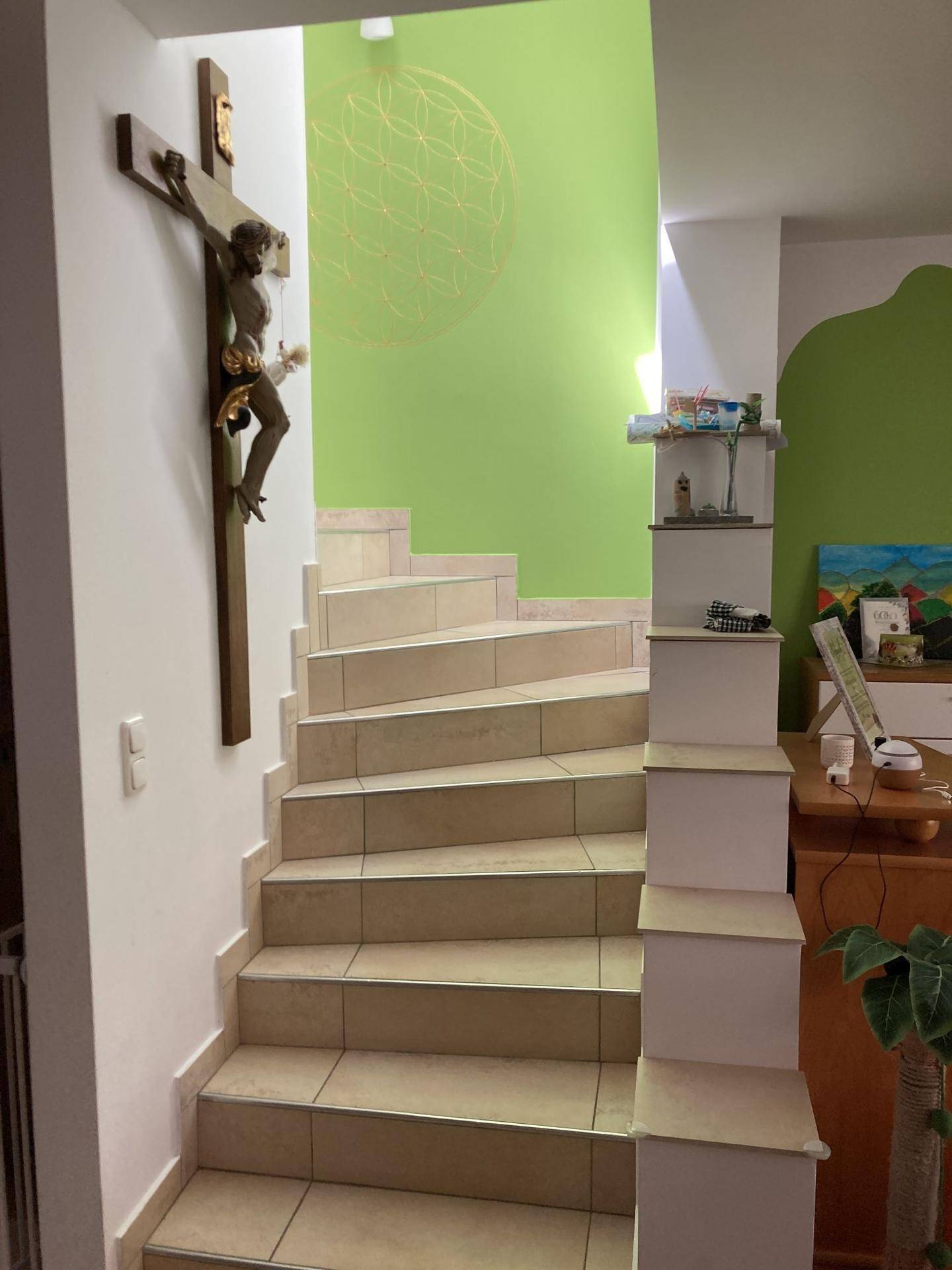 Treppenaufgang mit Fliesenstufen und heller Wandgestaltung, verziert mit einem Kreuz.