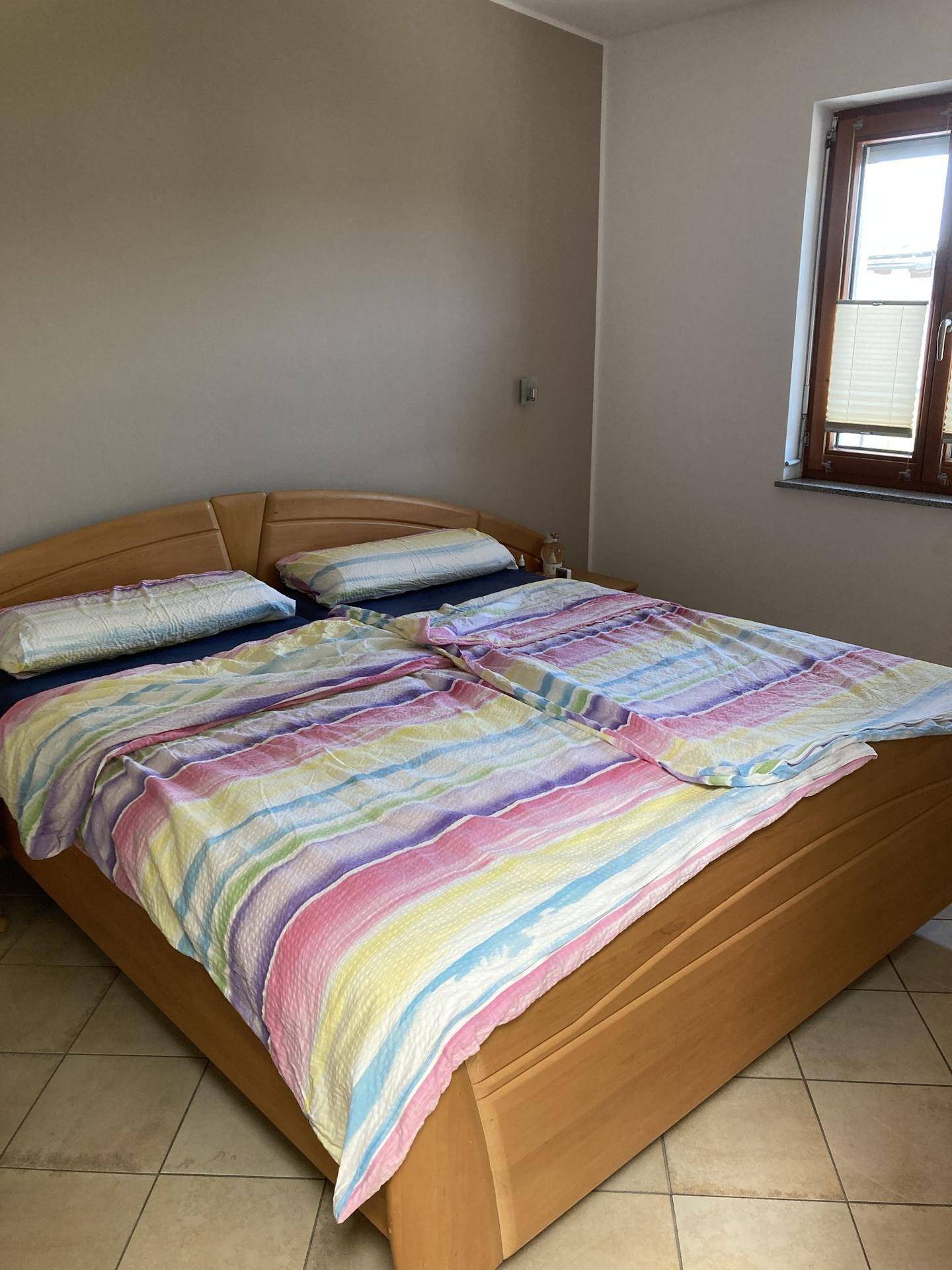 Schlafzimmer mit Doppelbett, bunten Bettdecken und gefliestem Boden.