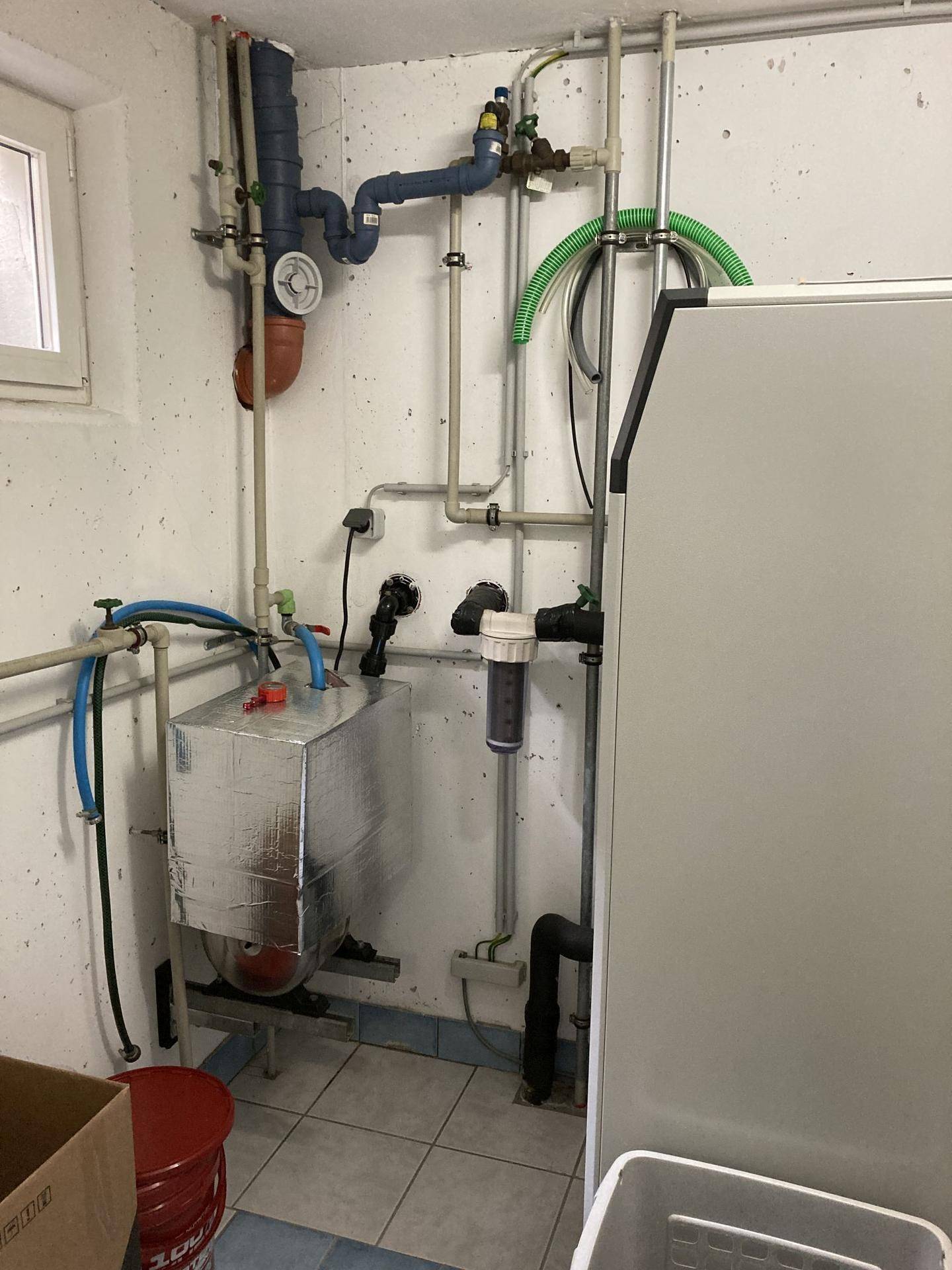 Technikraum mit komplexem Rohrsystem, Wasserfilter und isoliertem Wassertank.