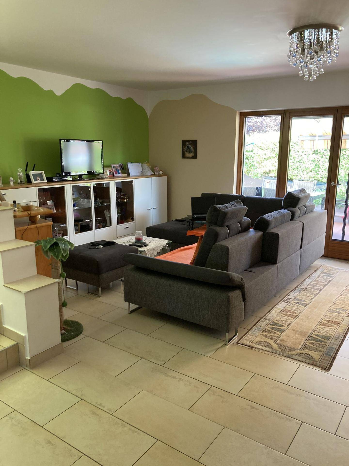 Geräumiges Wohnzimmer mit großem Sofa, Fliesenboden und Zugang zum Garten.