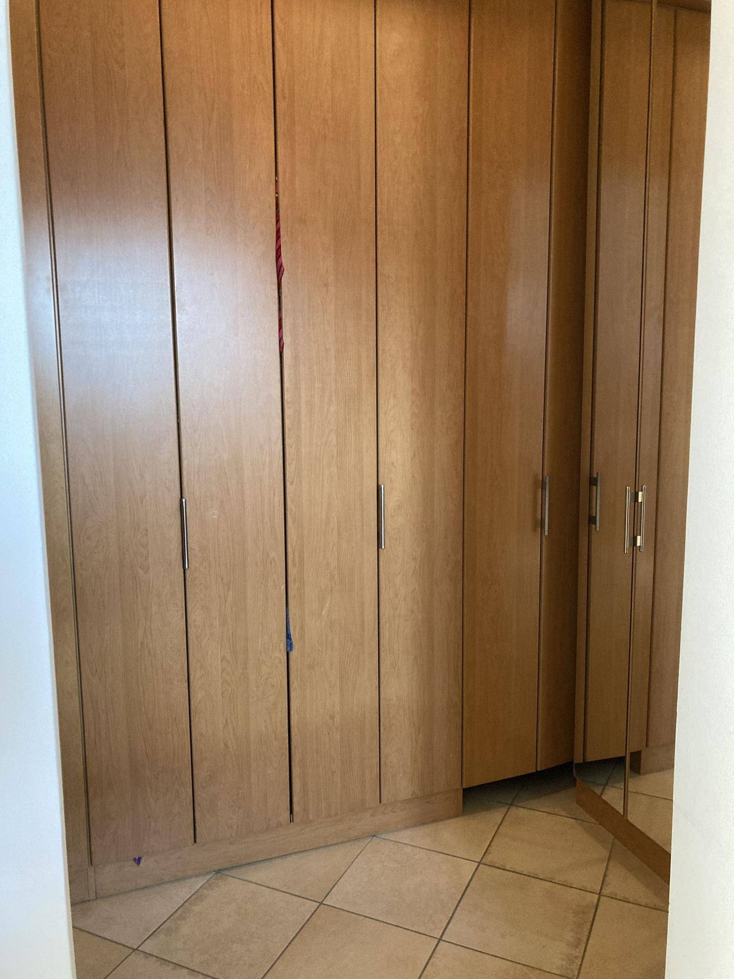 Schlafzimmer mit raumhohen Einbauschränken aus hellem Holz und Fliesenboden.