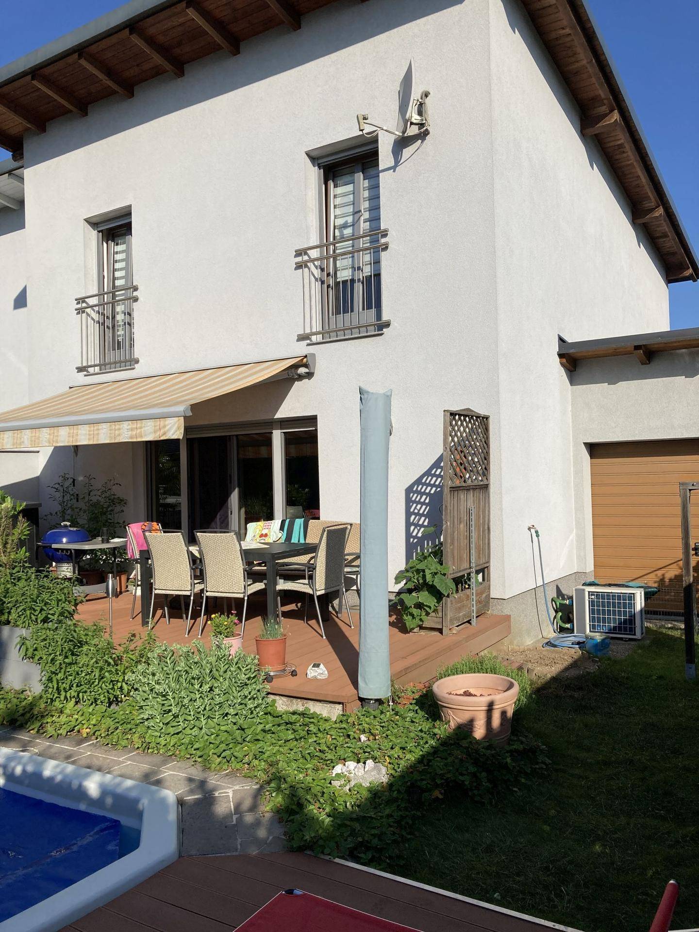 Terrasse mit Gartenmöbeln, Markise und Blick auf den Poolbereich im Garten.