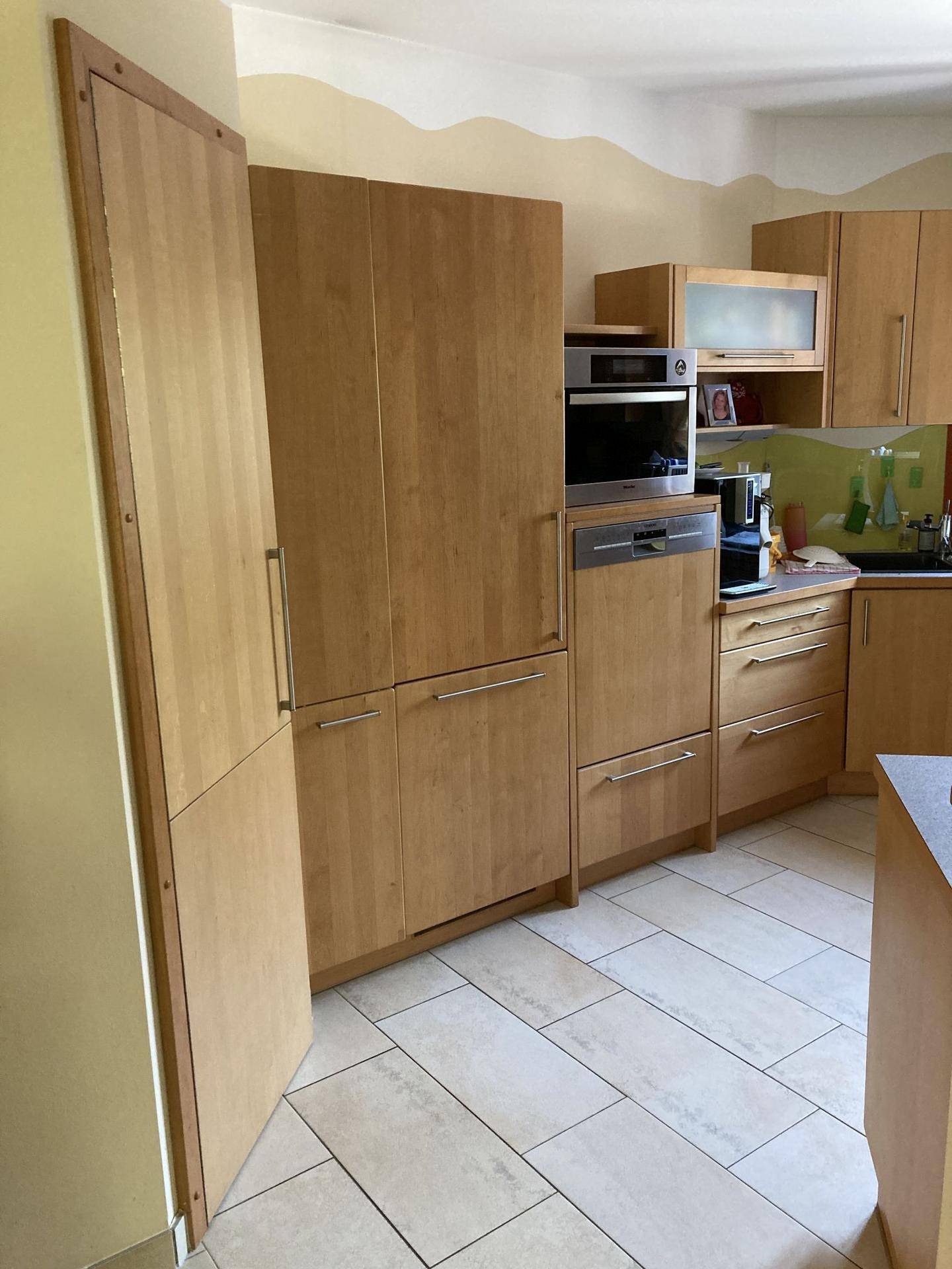 Einbauküche aus hellem Holz mit integriertem Kühlschrank und modernen Geräten.