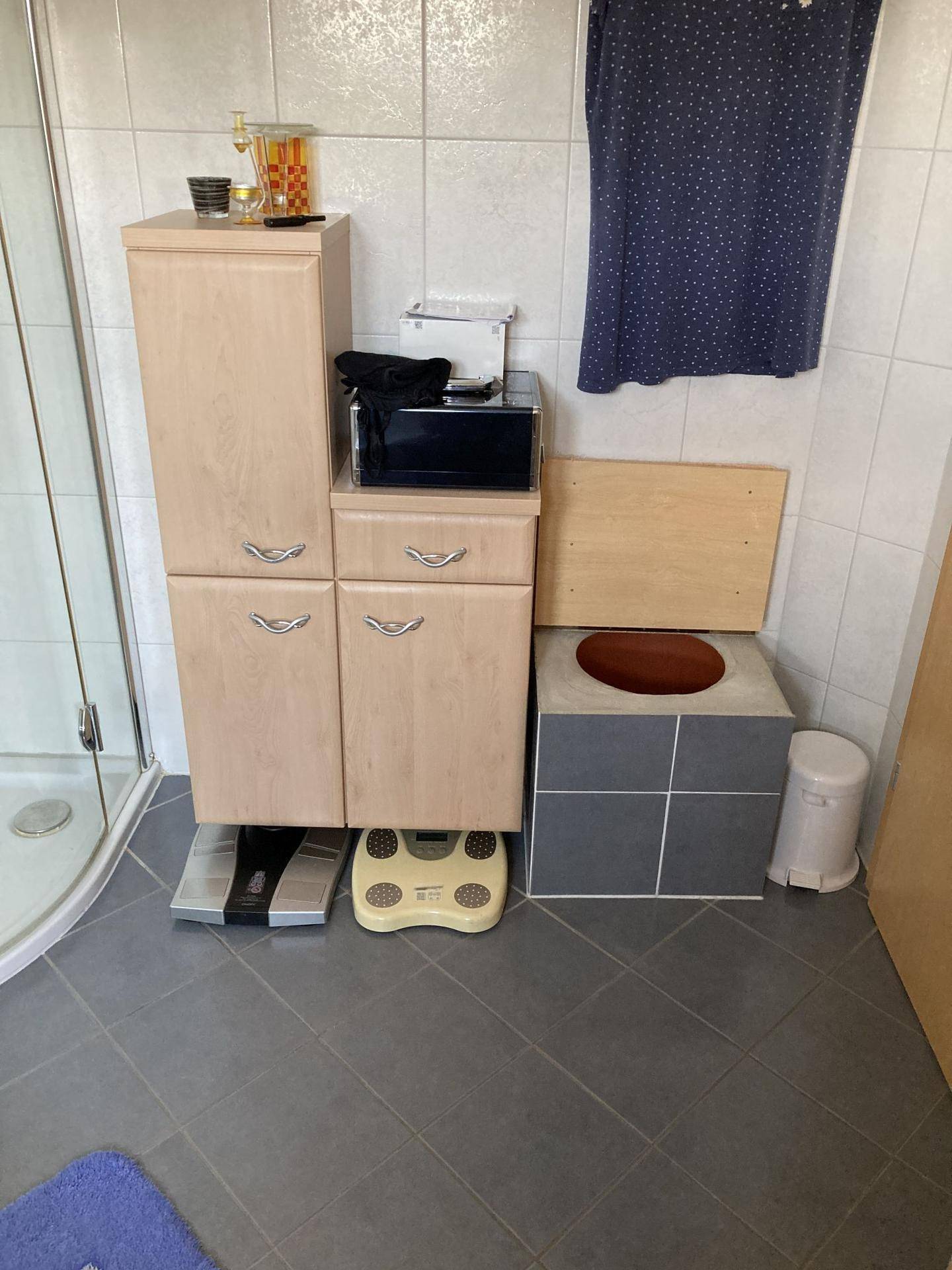 Badezimmer mit Duschbereich, Schränken und einem Hocker.