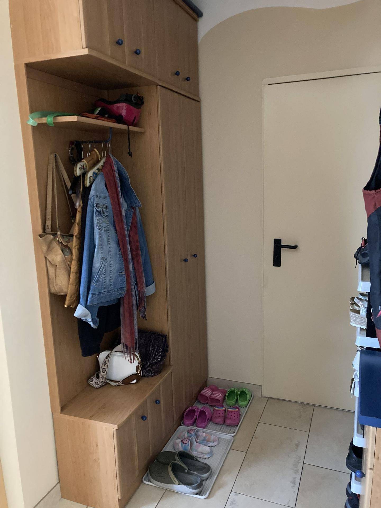 Flur mit Garderobenschrank aus hellem Holz und Ablageflächen für Schuhe und Kleidung.