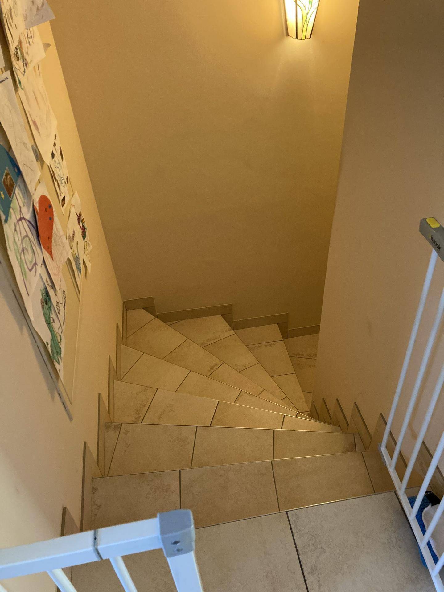 Treppenabgang mit Fliesenstufen und Kindersicherung am Geländer.