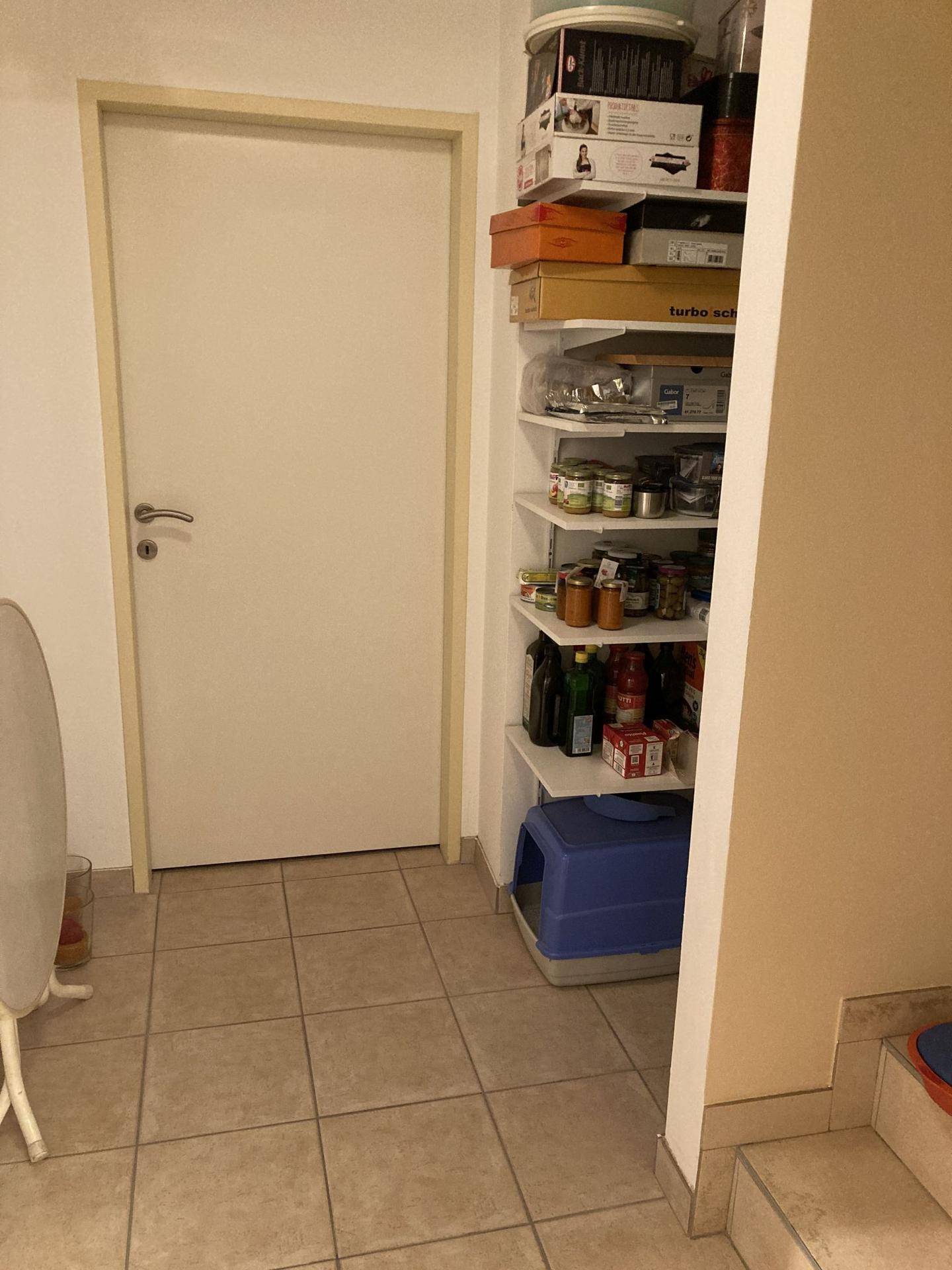 Abstellraum oder Speisekammer mit Regalen voller Vorräte und einer Tür.