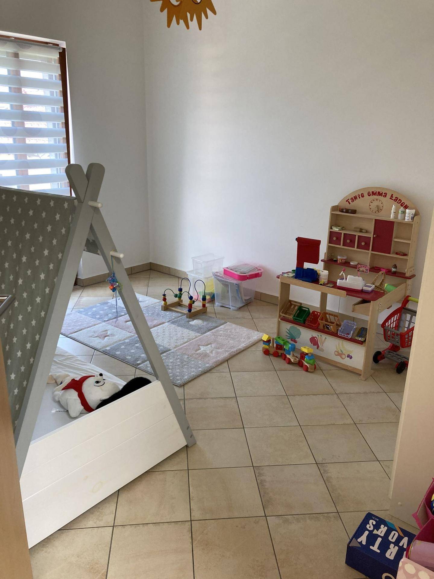 Kinderzimmer mit Spielbereich, Tipi-Zelt und Spielküche auf gefliestem Boden.